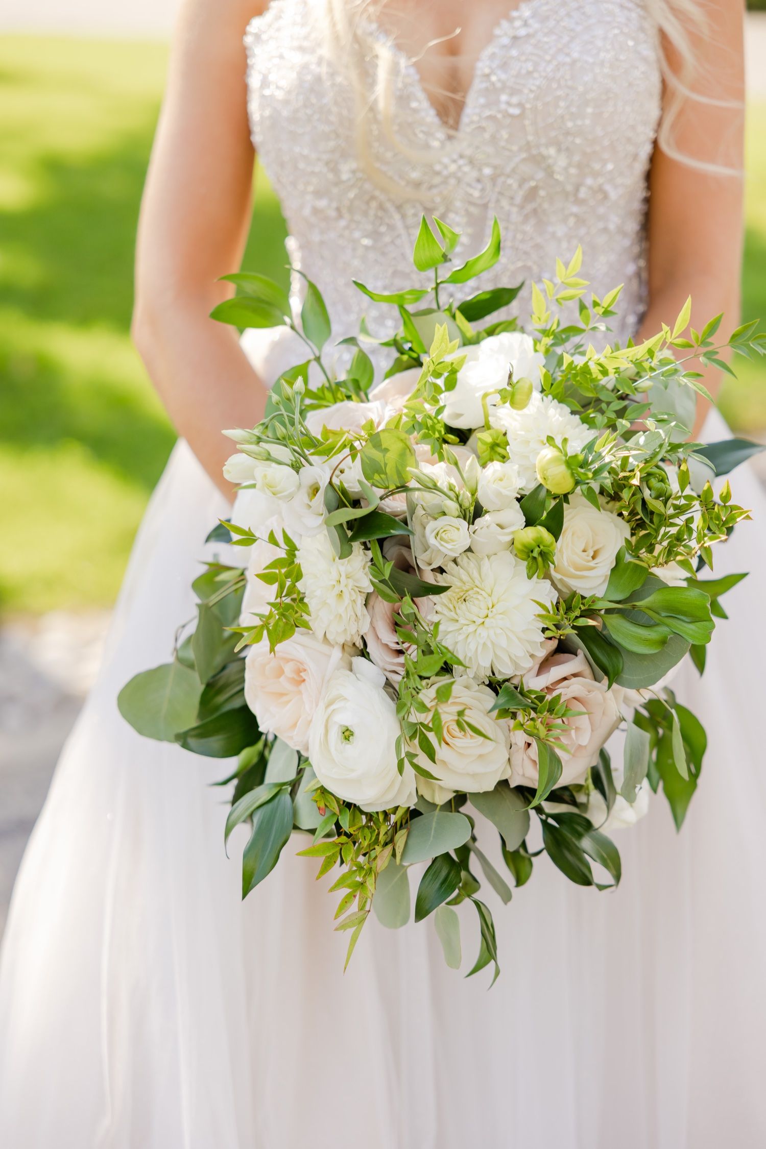 Close-up of an elegant white and green wedding bouquet with roses and eucalyptus against a bridal gown.