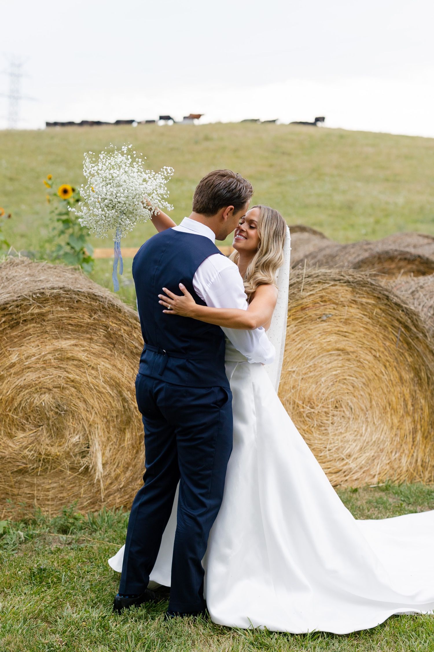 A romantic wedding portrait with the couple embracing by hay bales in a rustic outdoor setting.