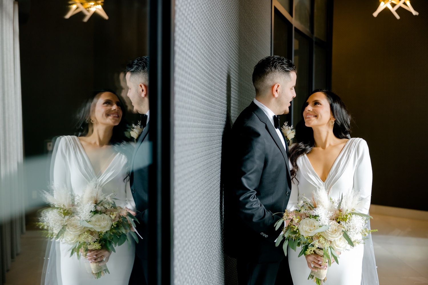 Elegant wedding couple shares joyful moments against a modern interior wall with beautiful natural light.