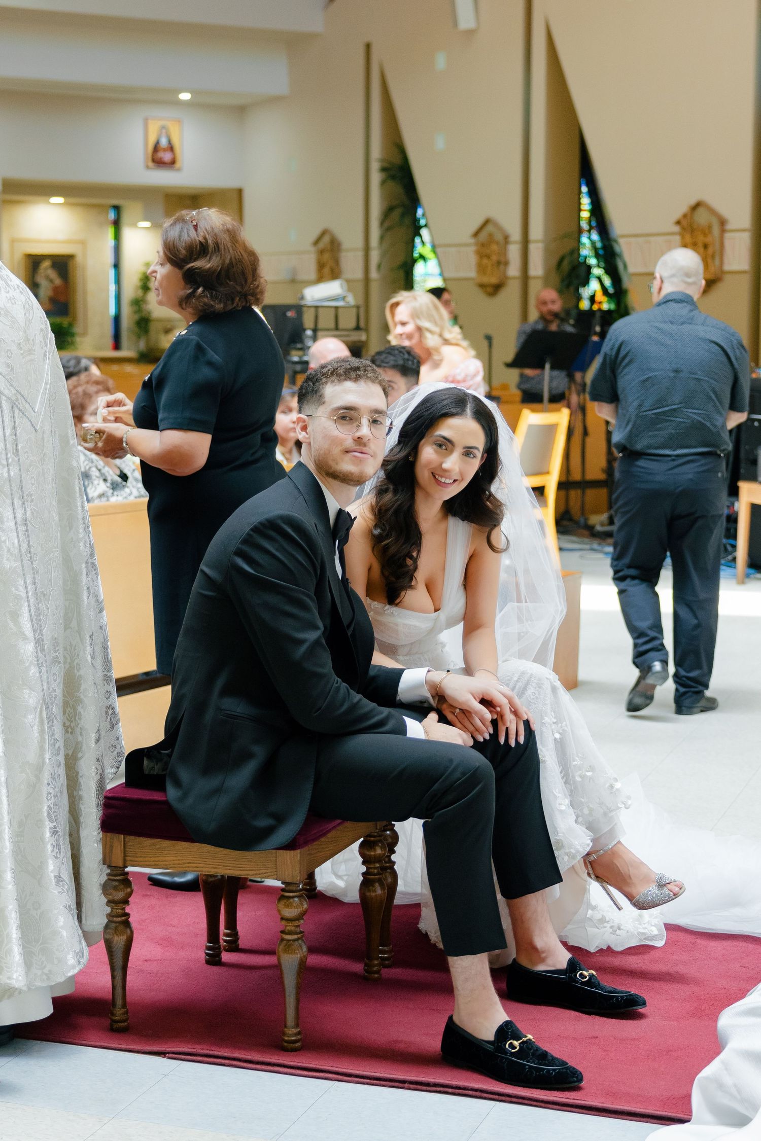 A newlywed couple sits on red chairs during their wedding ceremony.