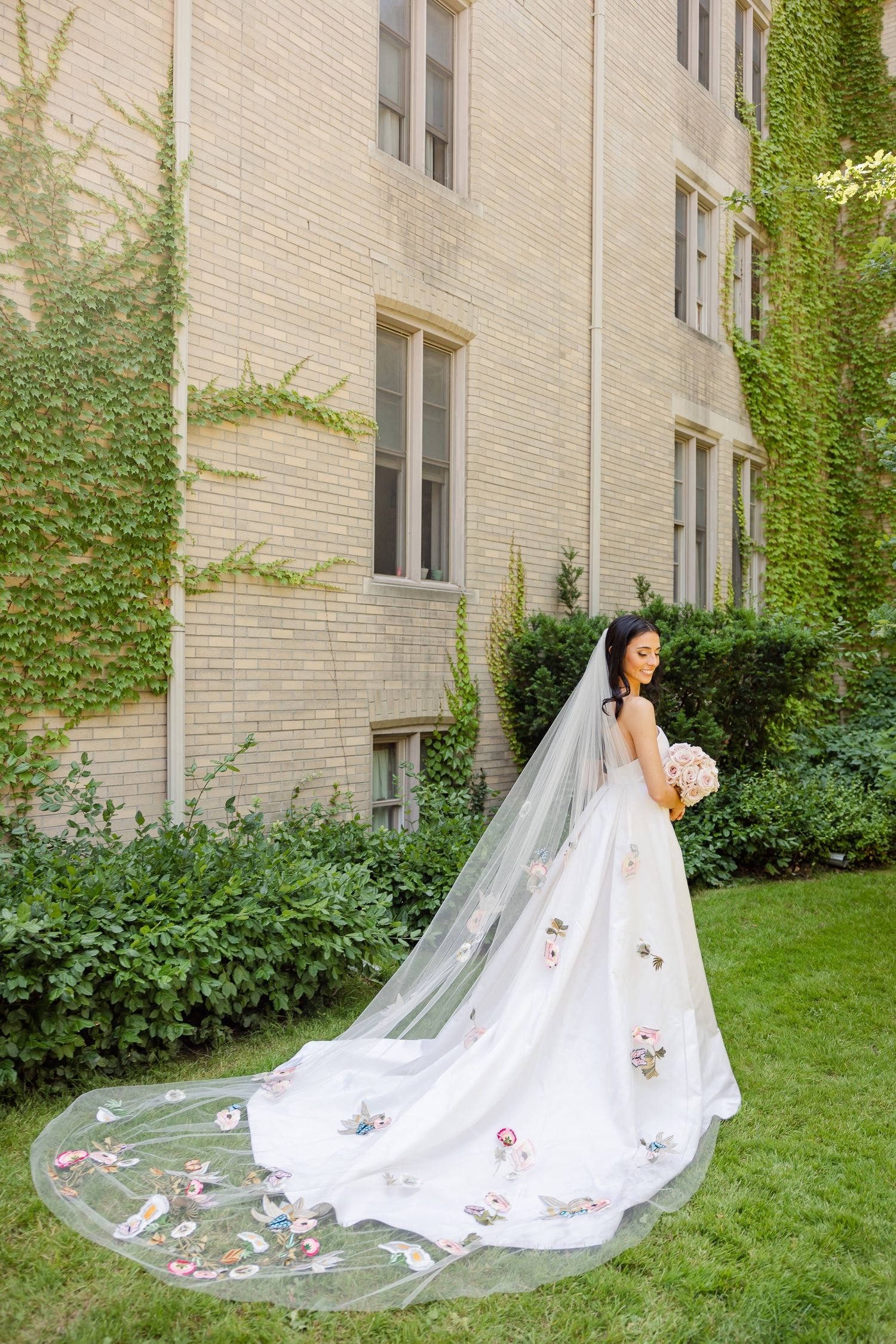 A stunning bridal portrait featuring an ornate floral-detailed veil and train against a garden backdrop.