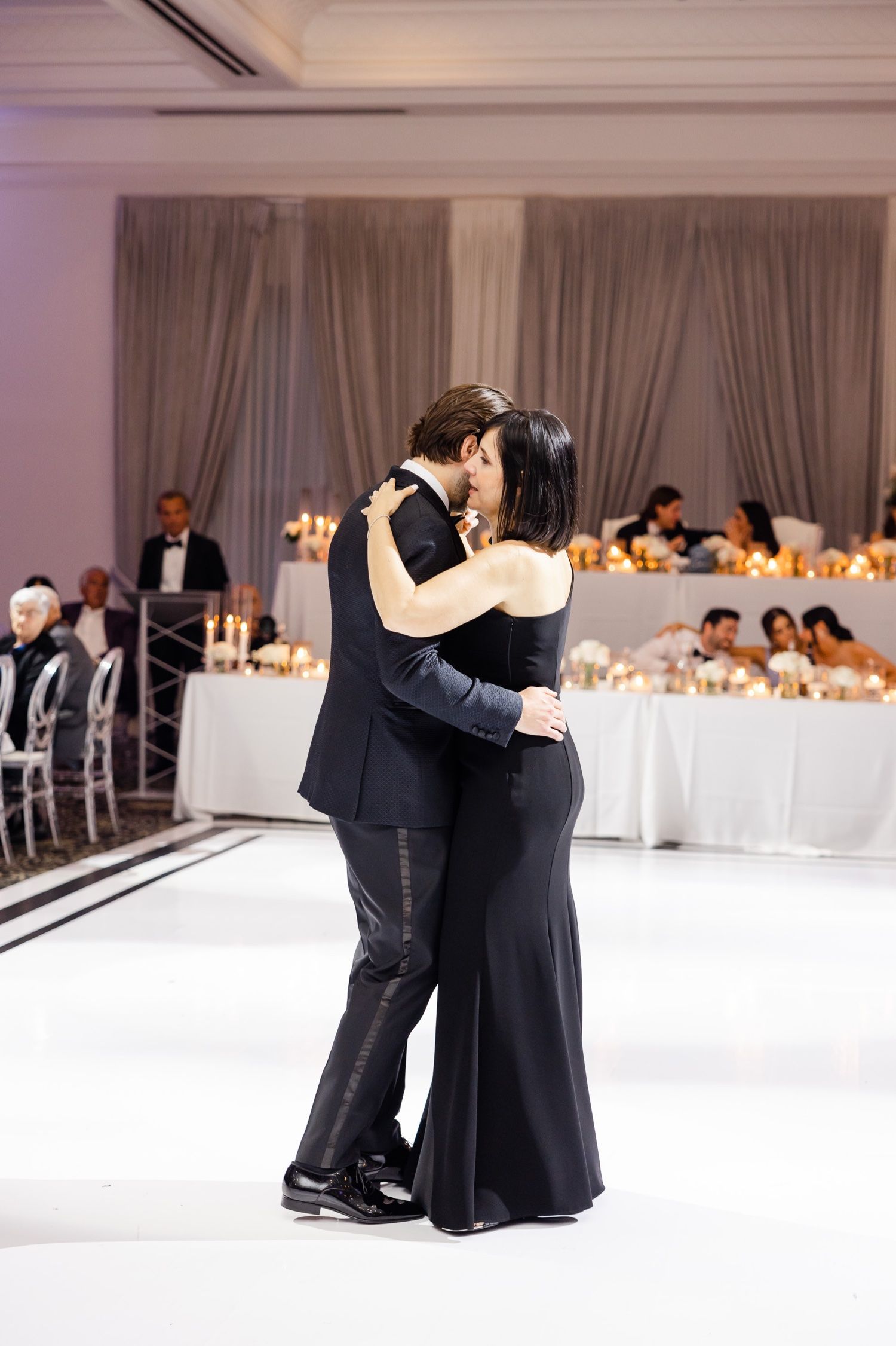 A slow dance embrace during a wedding reception with elegant table settings in the background.