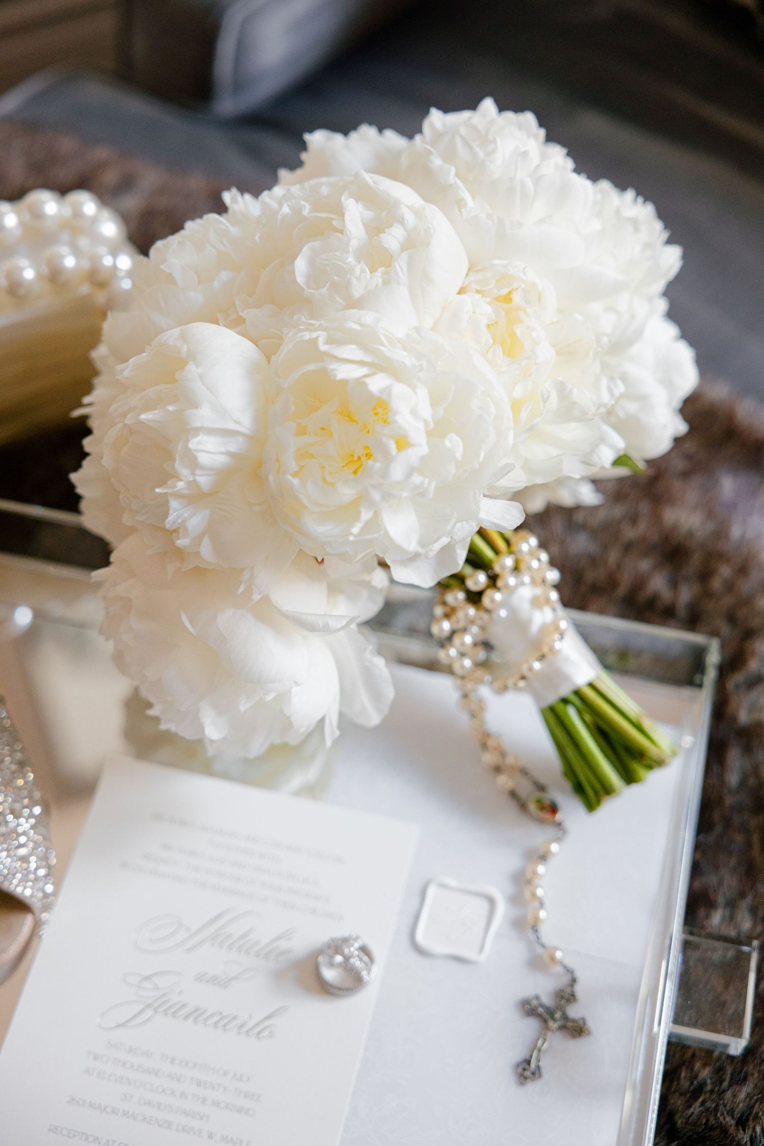 White peony bridal bouquet with pearl-wrapped stem laying on wedding invitation.