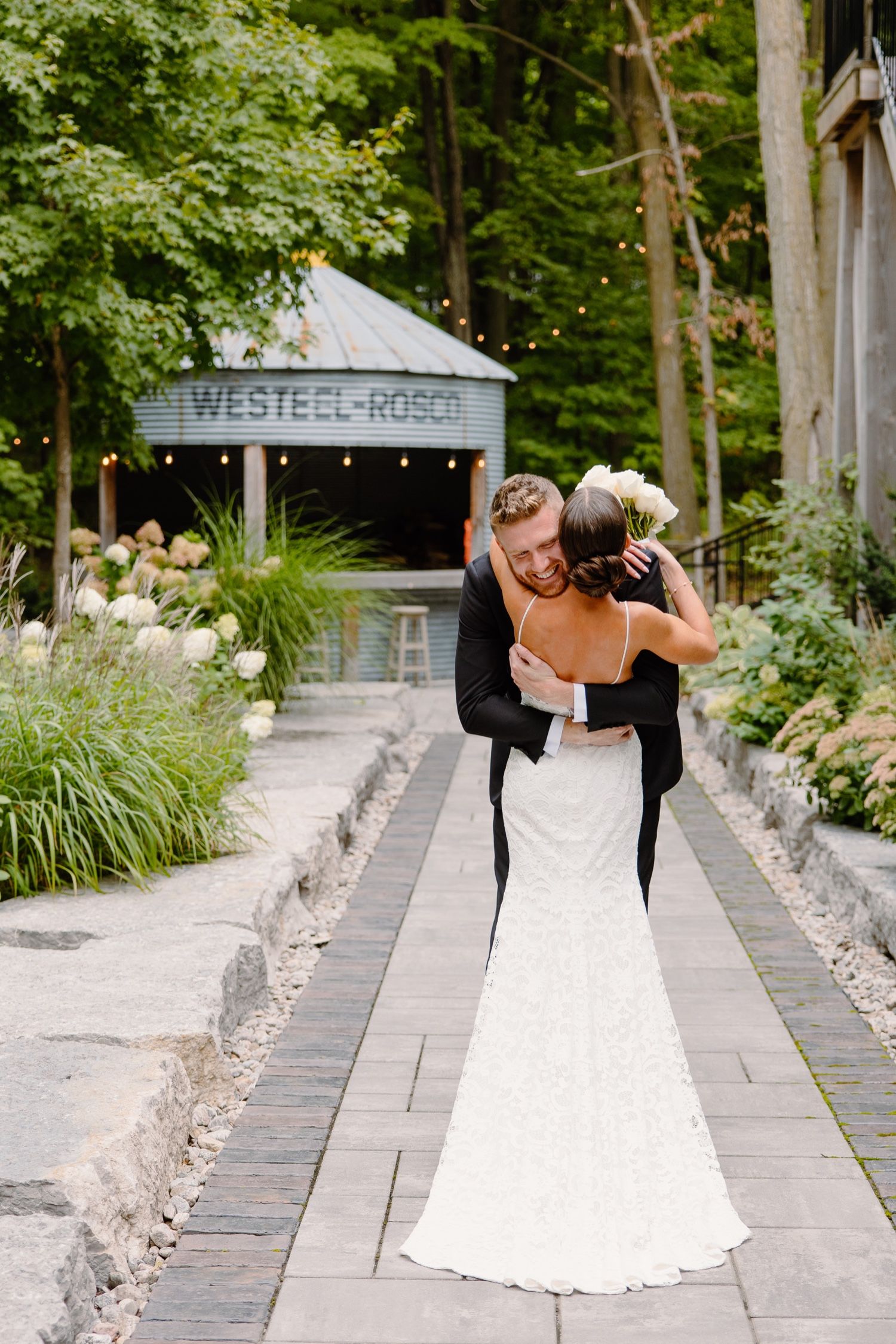 Newlyweds share an intimate moment on a stone walkway surrounded by lush garden landscaping.