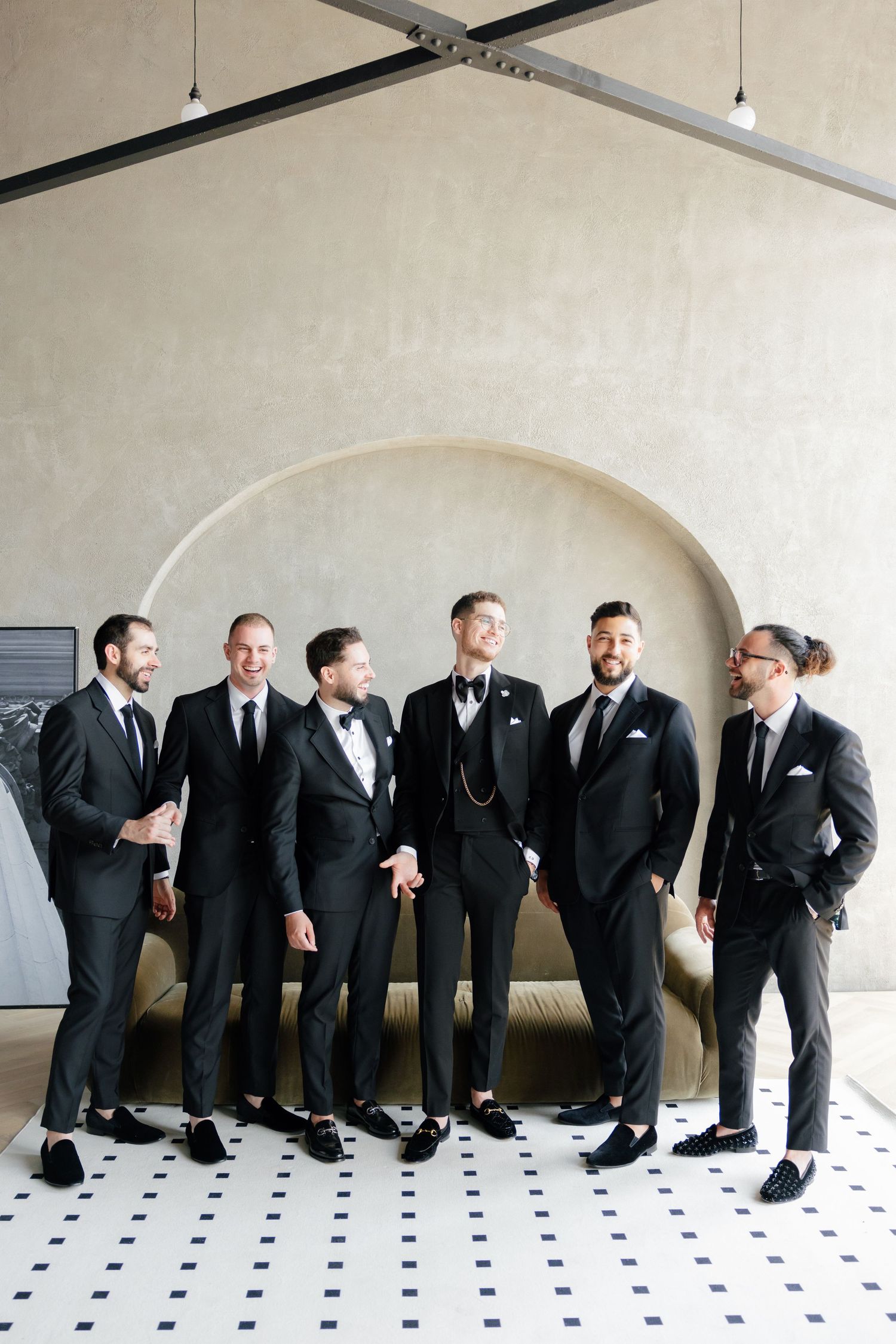 Candid shot of groomsmen laughing and interacting in formal wear against a modern backdrop.