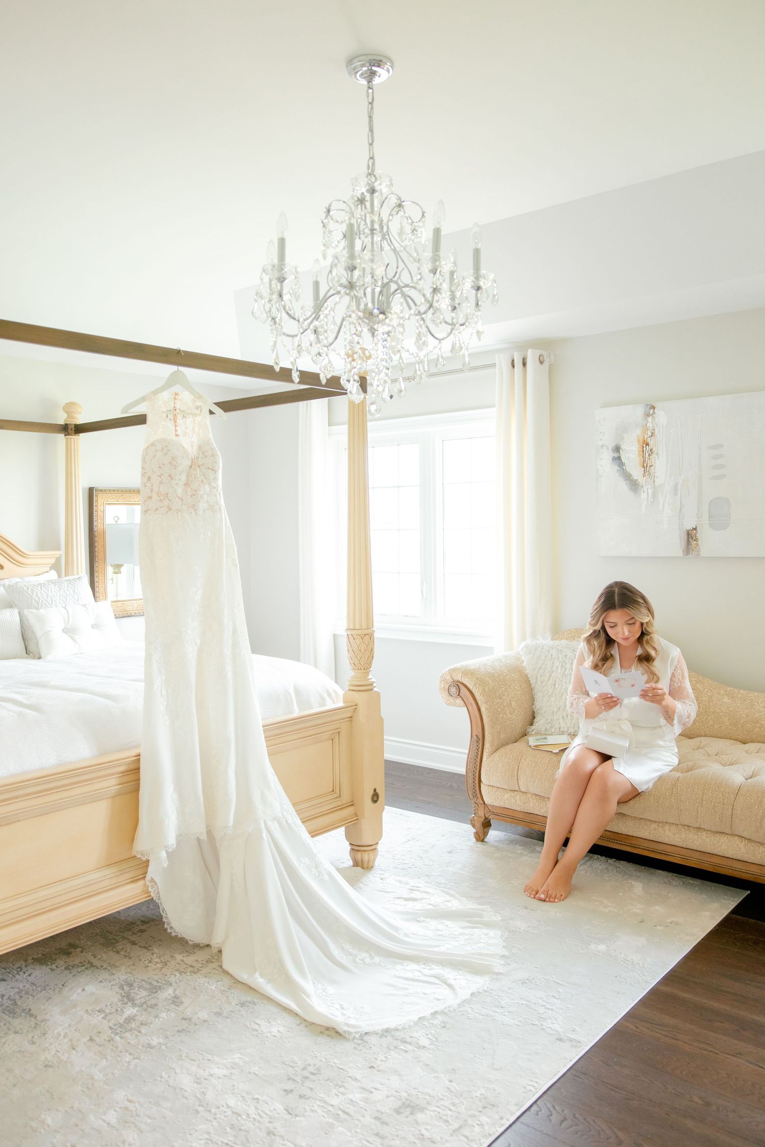 Luxury bedroom with crystal chandelier, four-poster bed, and white wedding dress on display.