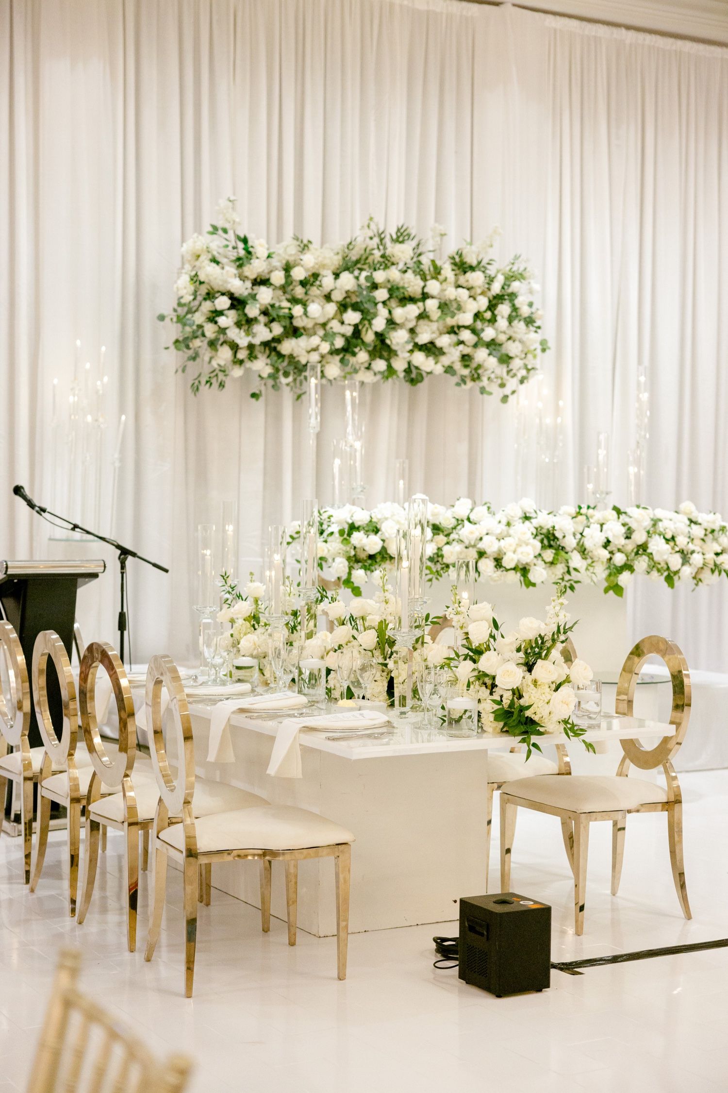 Luxurious white and gold wedding reception decor with suspended floral installations.