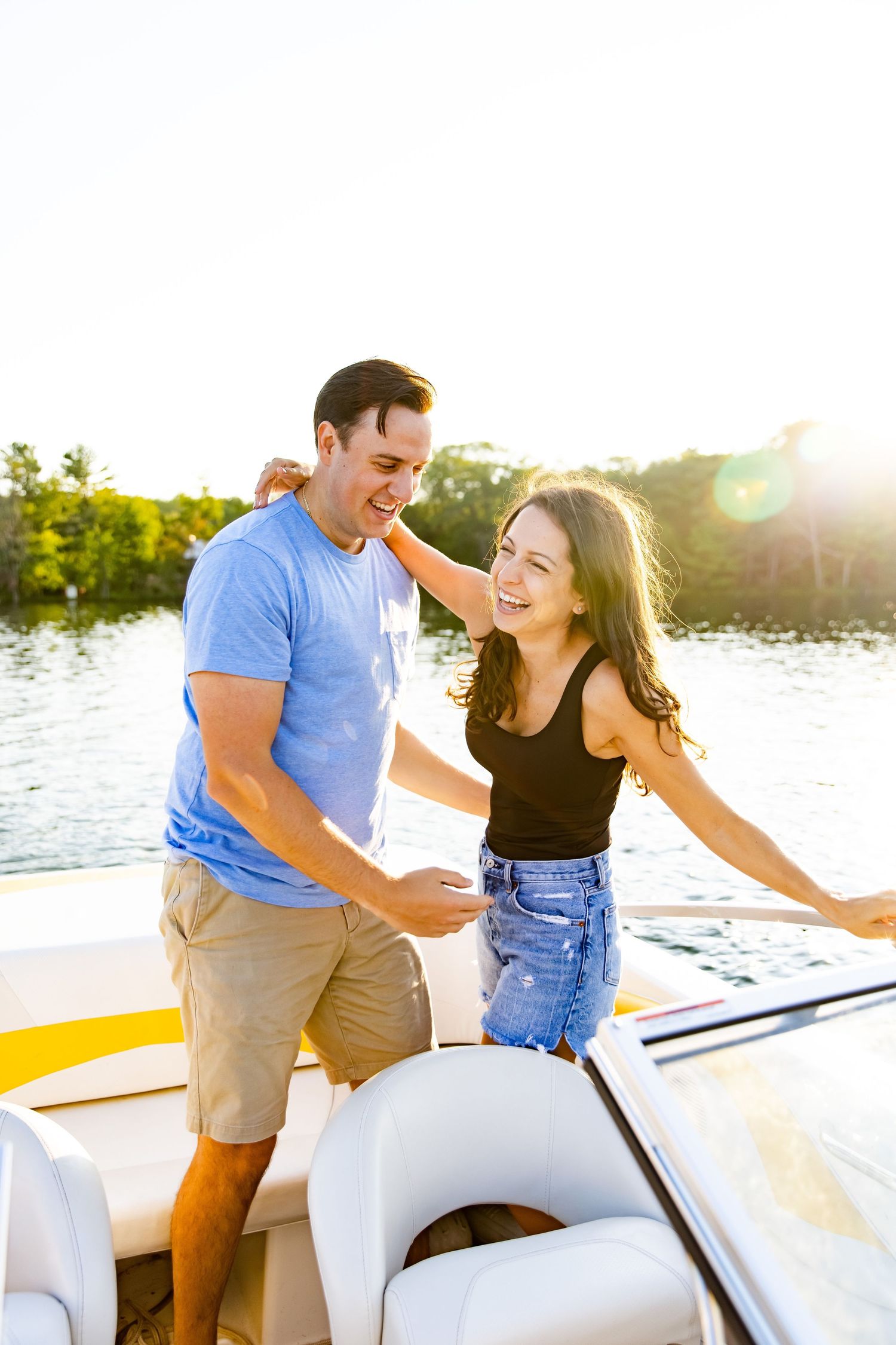 Happy couple dancing and laughing on boat deck in summer sunlight.