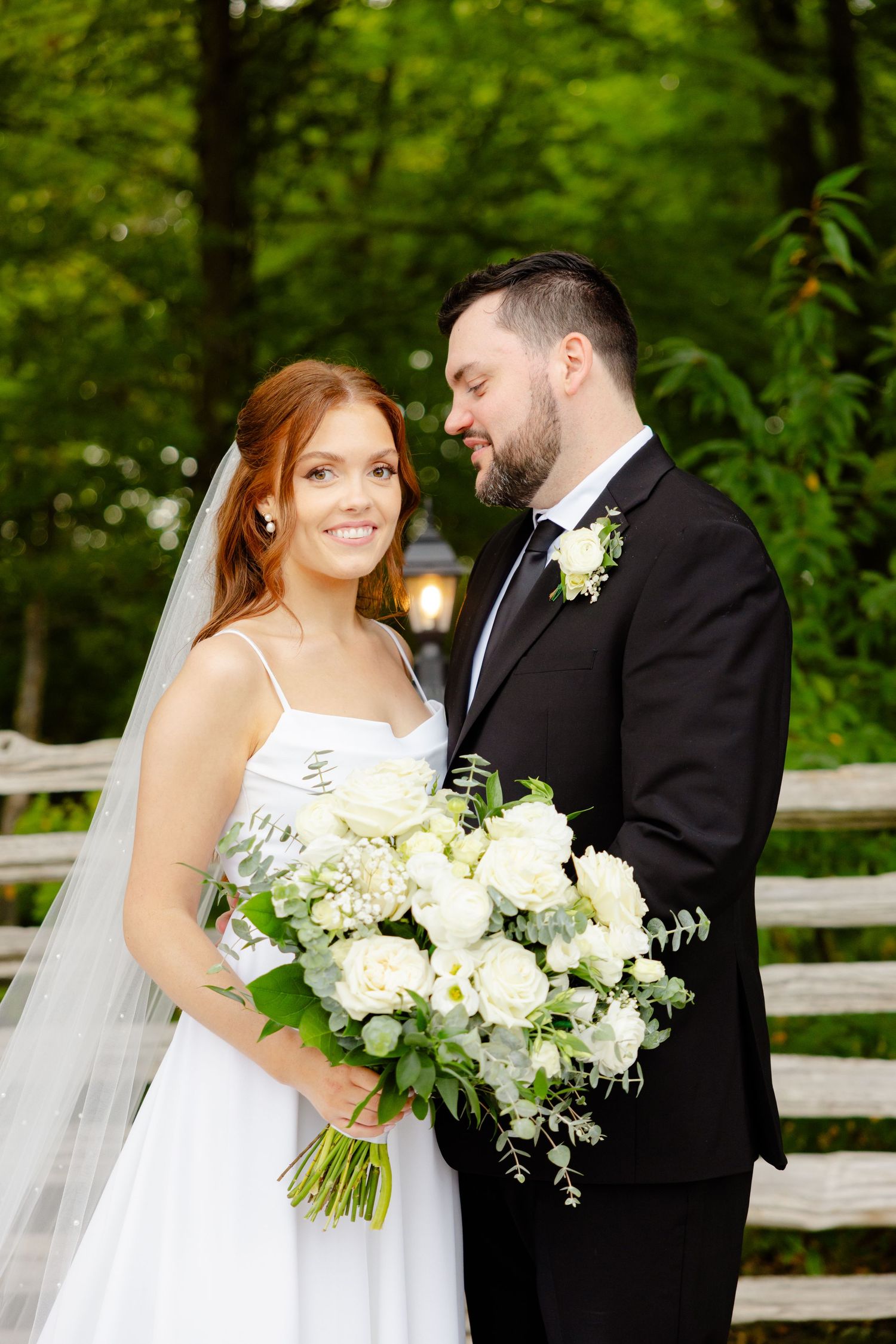 A close-up of newlyweds sharing an intimate moment with a stunning white bouquet against greenery.