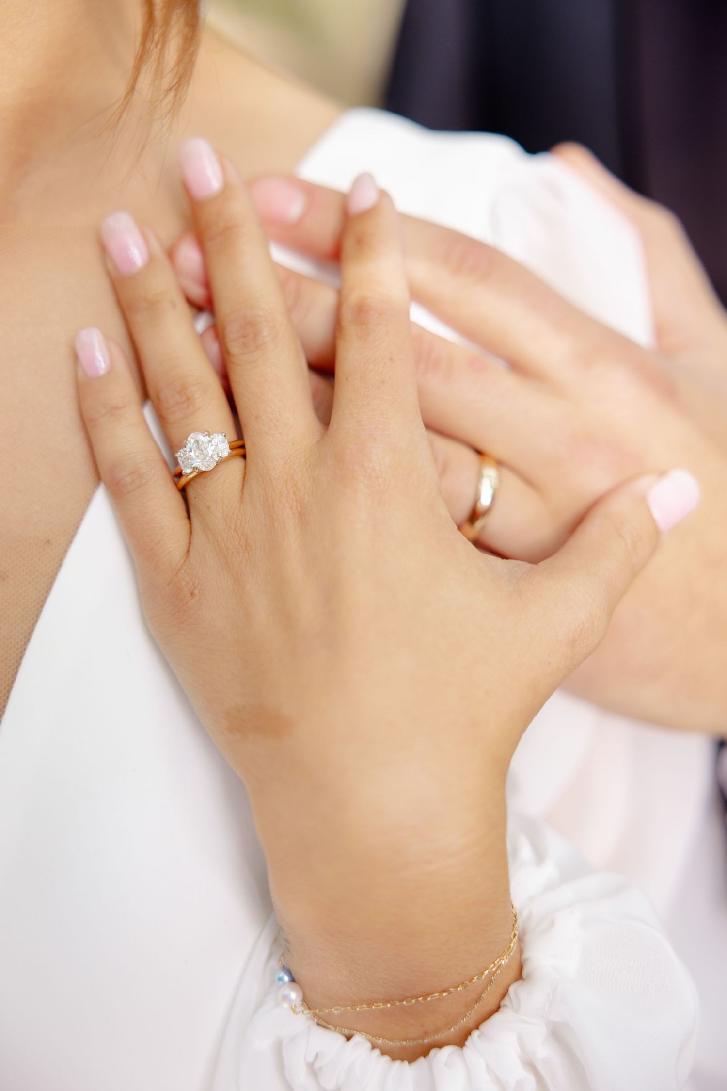 Close-up of bride's hands showing diamond engagement ring and wedding band with manicured nails.