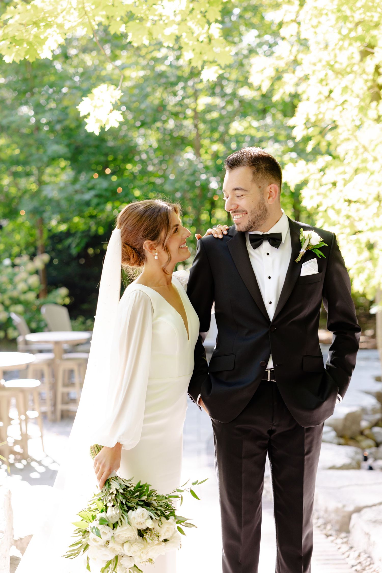 A joyful wedding moment captured outdoors with elegant white bouquet and classic black tuxedo in natural light.