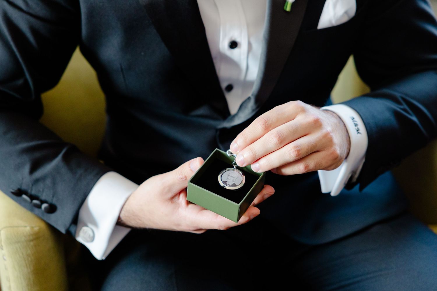 Detailed view of hands holding a small box while wearing formal wedding attire.