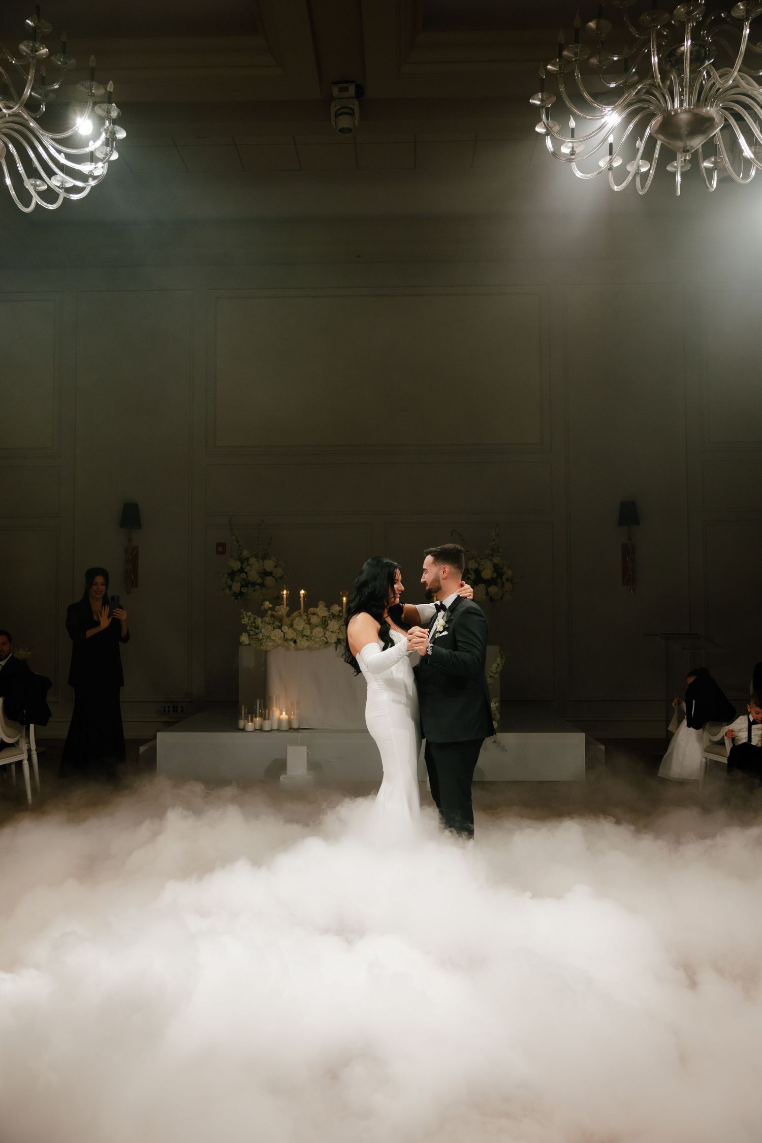Newlyweds dance on a misty dance floor under crystal chandeliers during their romantic reception.
