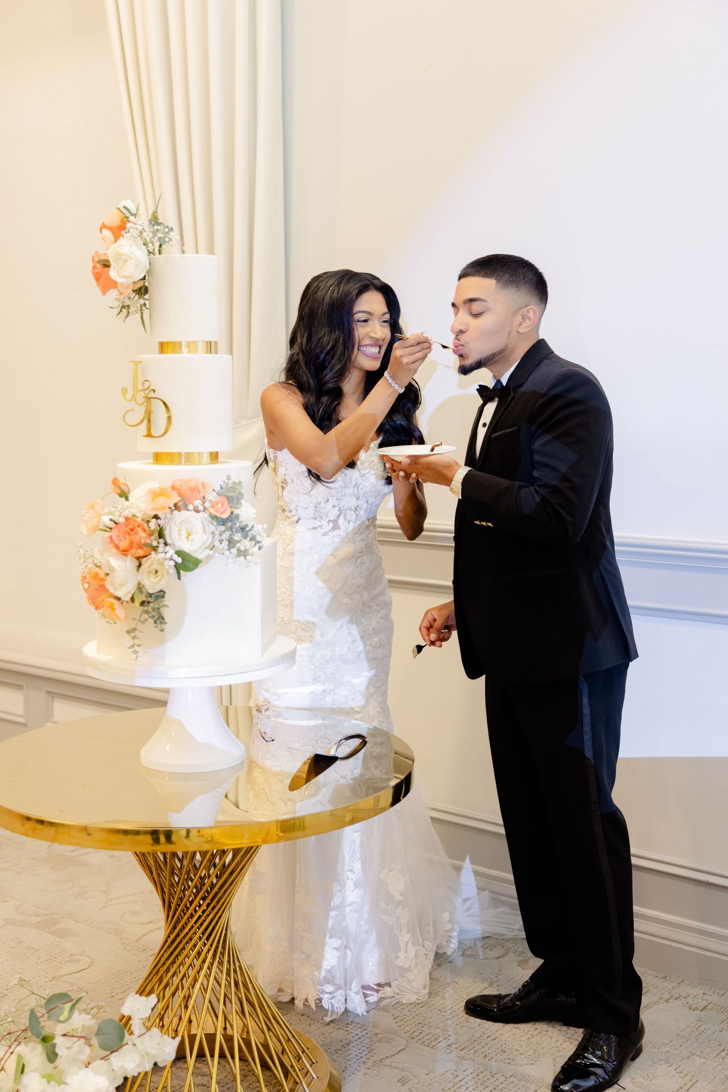 A couple shares a joyful moment while cutting their elegant white and peach floral wedding cake.