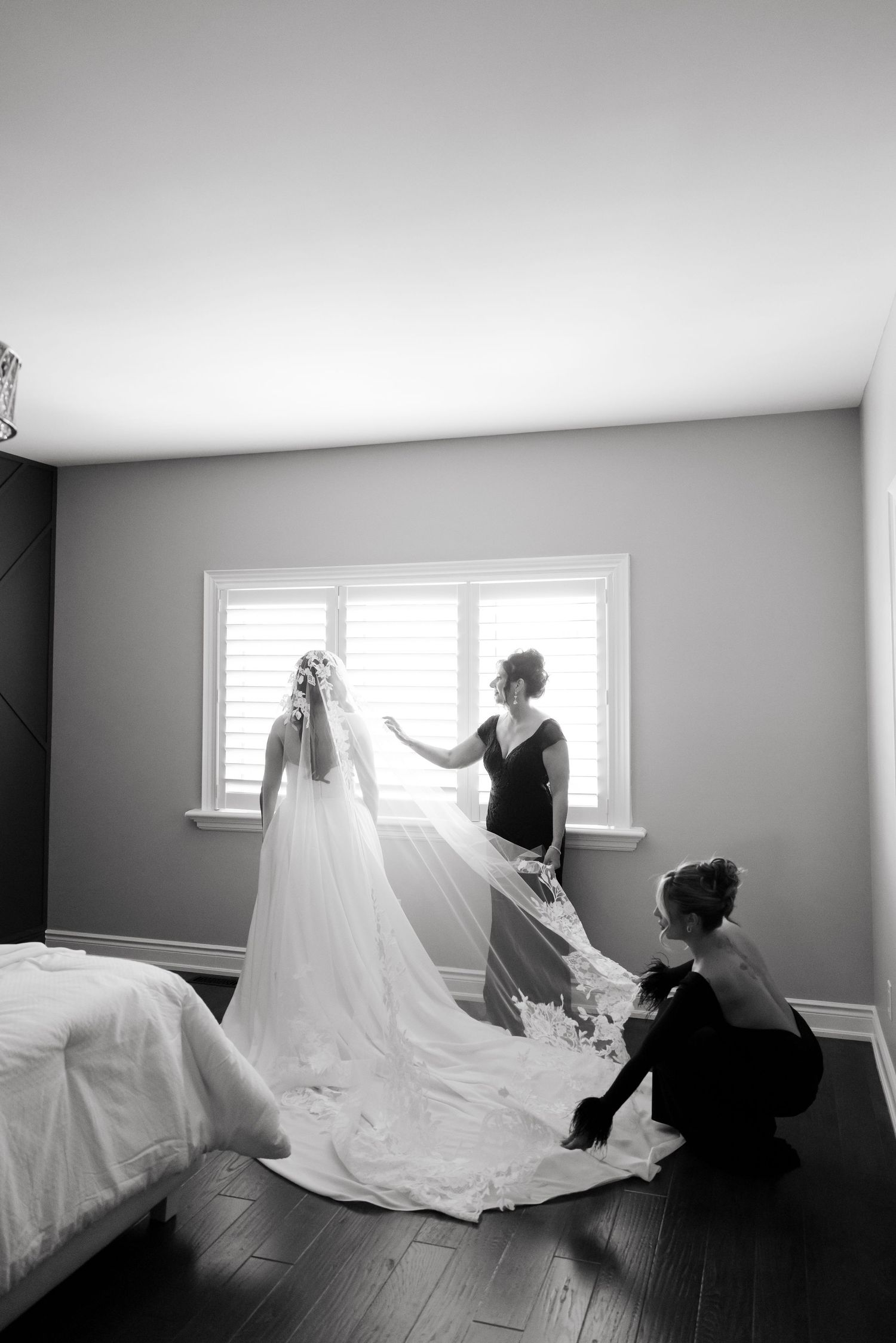 Black and white photo of wedding dress preparations with attendants adjusting the long flowing train.