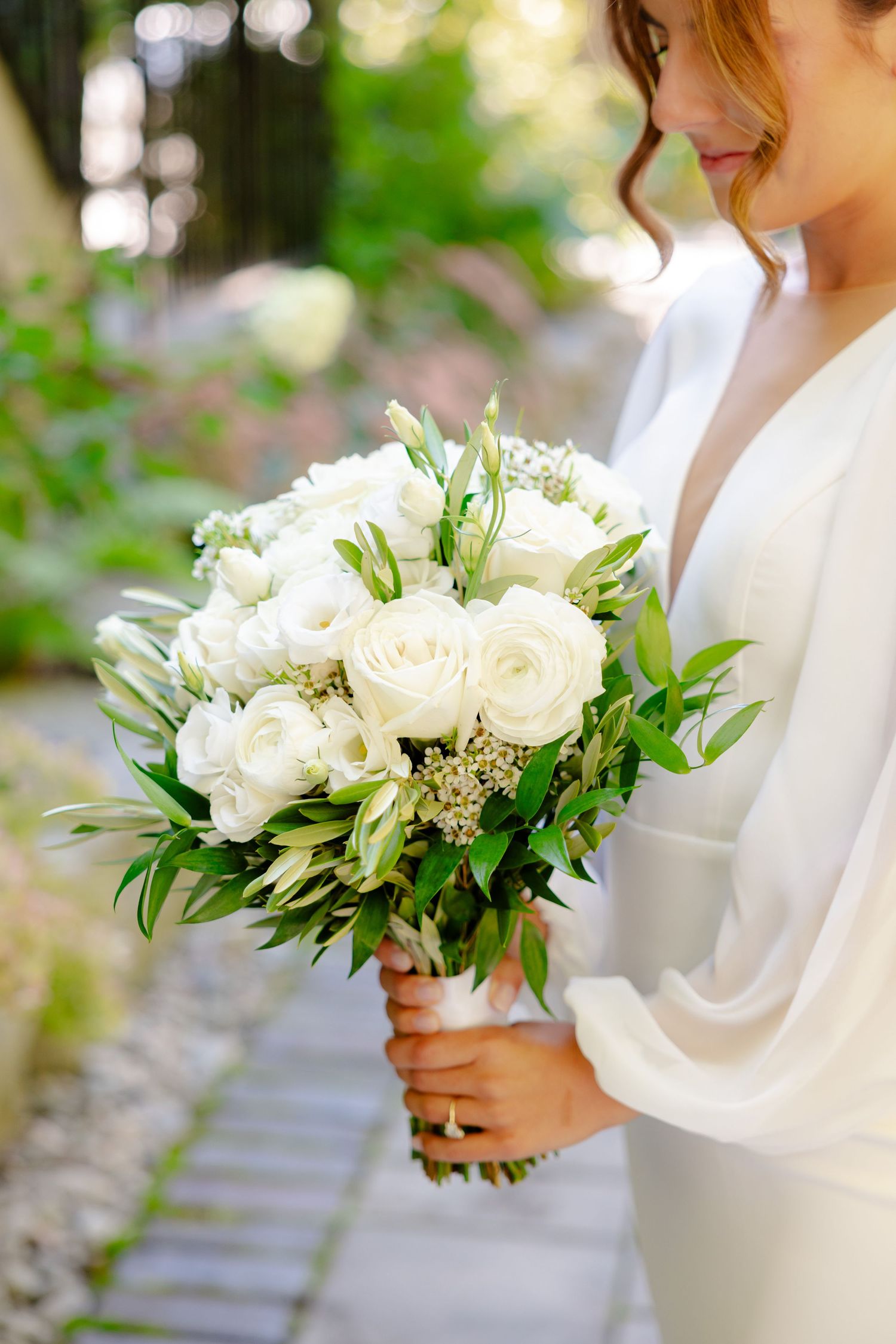 Close-up of white rose and greenery wedding bouquet held by bride in long-sleeved dress.