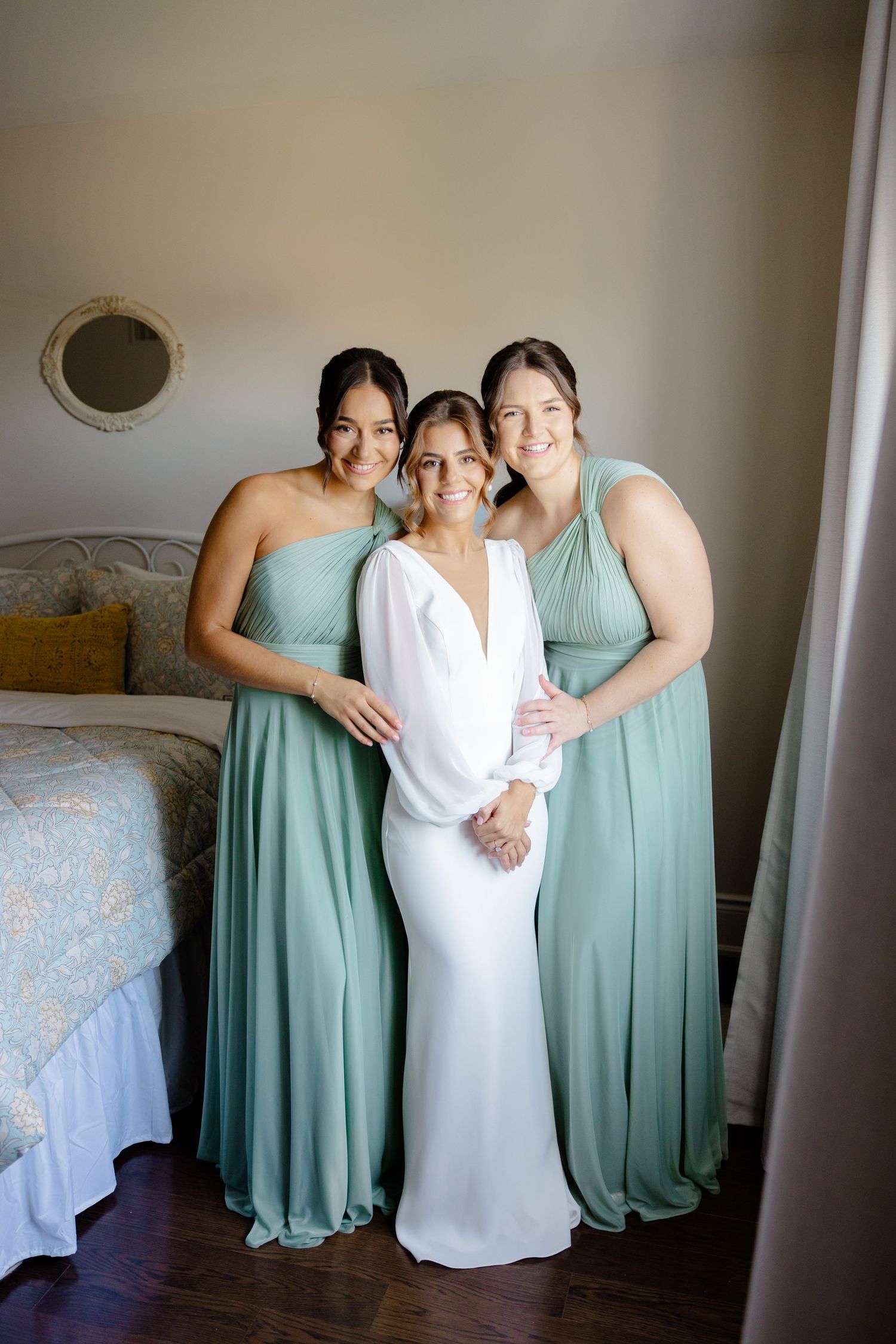 Wedding party poses in a bedroom, featuring mint green bridesmaid dresses and a sleek white bridal gown.