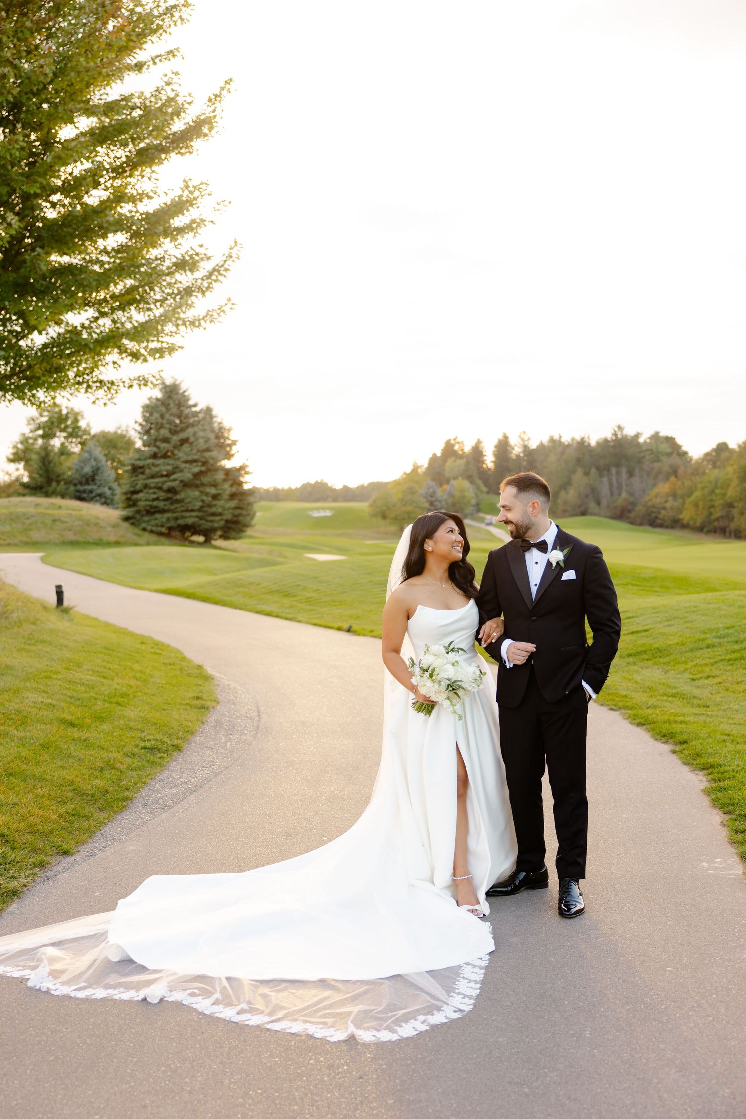 A wedding couple walking together on a curved path with rolling hills and evergreen trees in the background.
