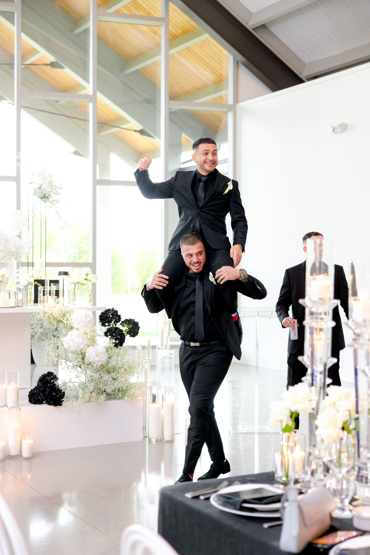 Wedding guests having fun with one person lifted on another's shoulders in a modern venue.