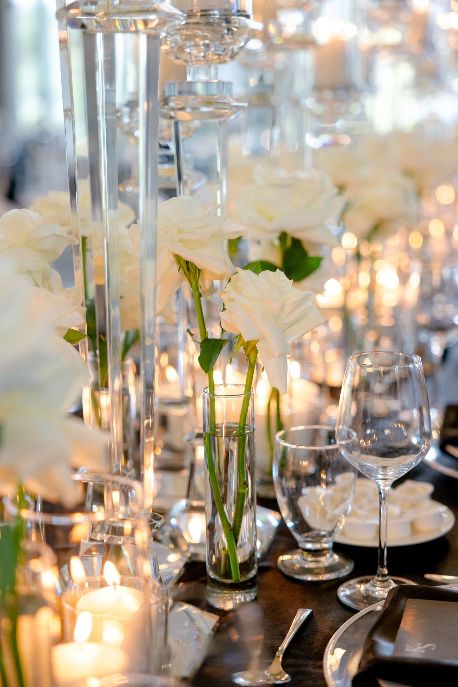 Detailed shot of wedding table decor with glass vessels, white flowers and candlelight.
