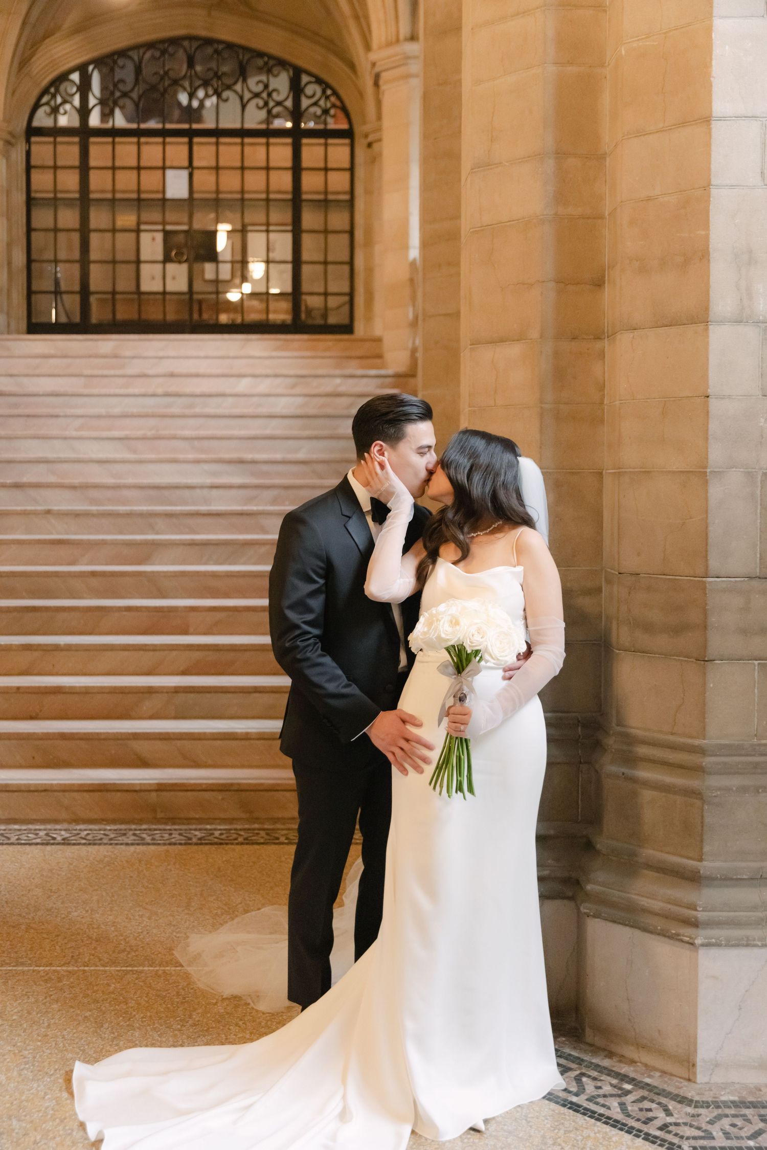 Intimate wedding portrait with couple against stone pillars and ornate staircase.