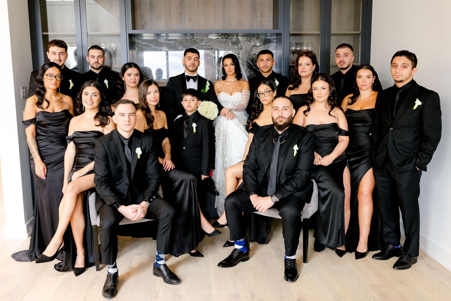 Wedding party in black formal attire poses together in a modern interior setting.