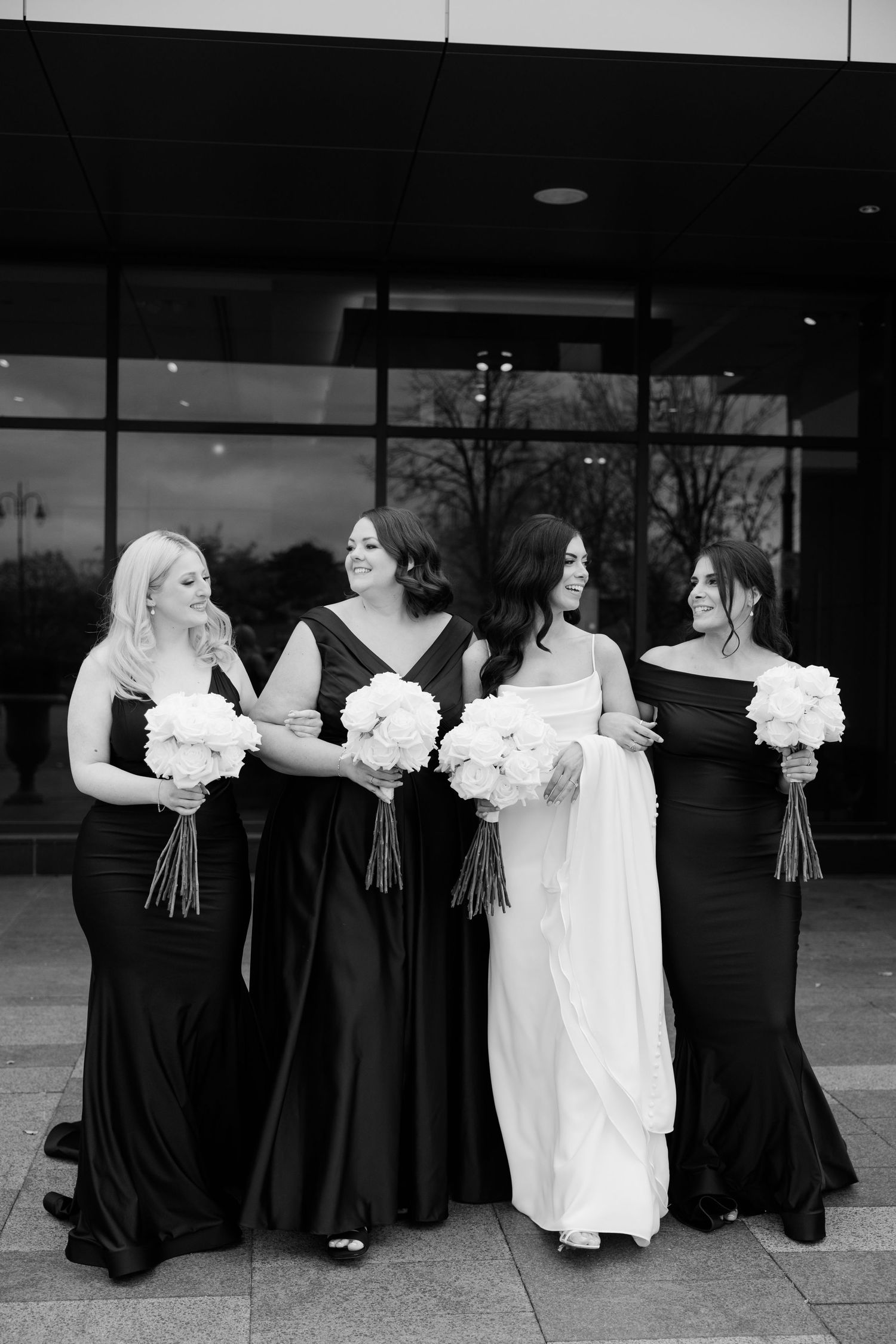 Black and white portrait of bridal party with bridesmaids in black gowns holding white bouquets.