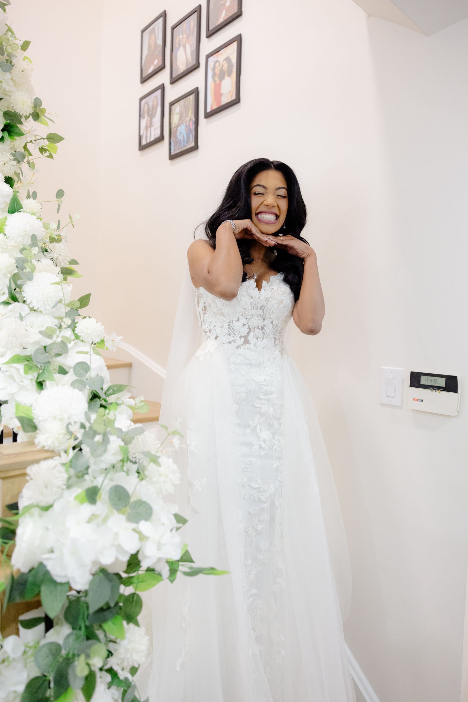 Bride laughs expressively in her white lace gown next to floral staircase decorations.