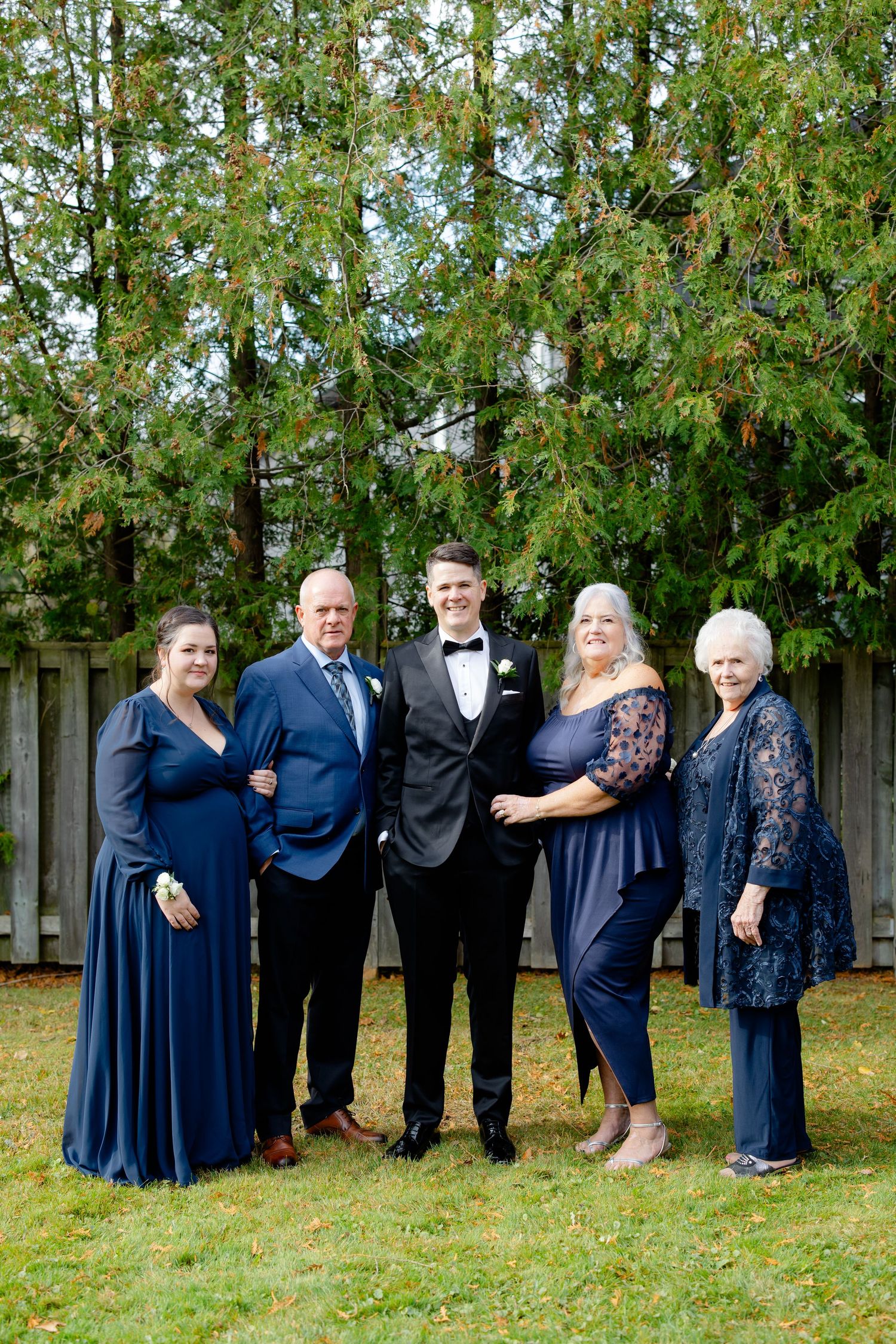 A group of five people dressed in formal navy and black attire pose together outdoors.