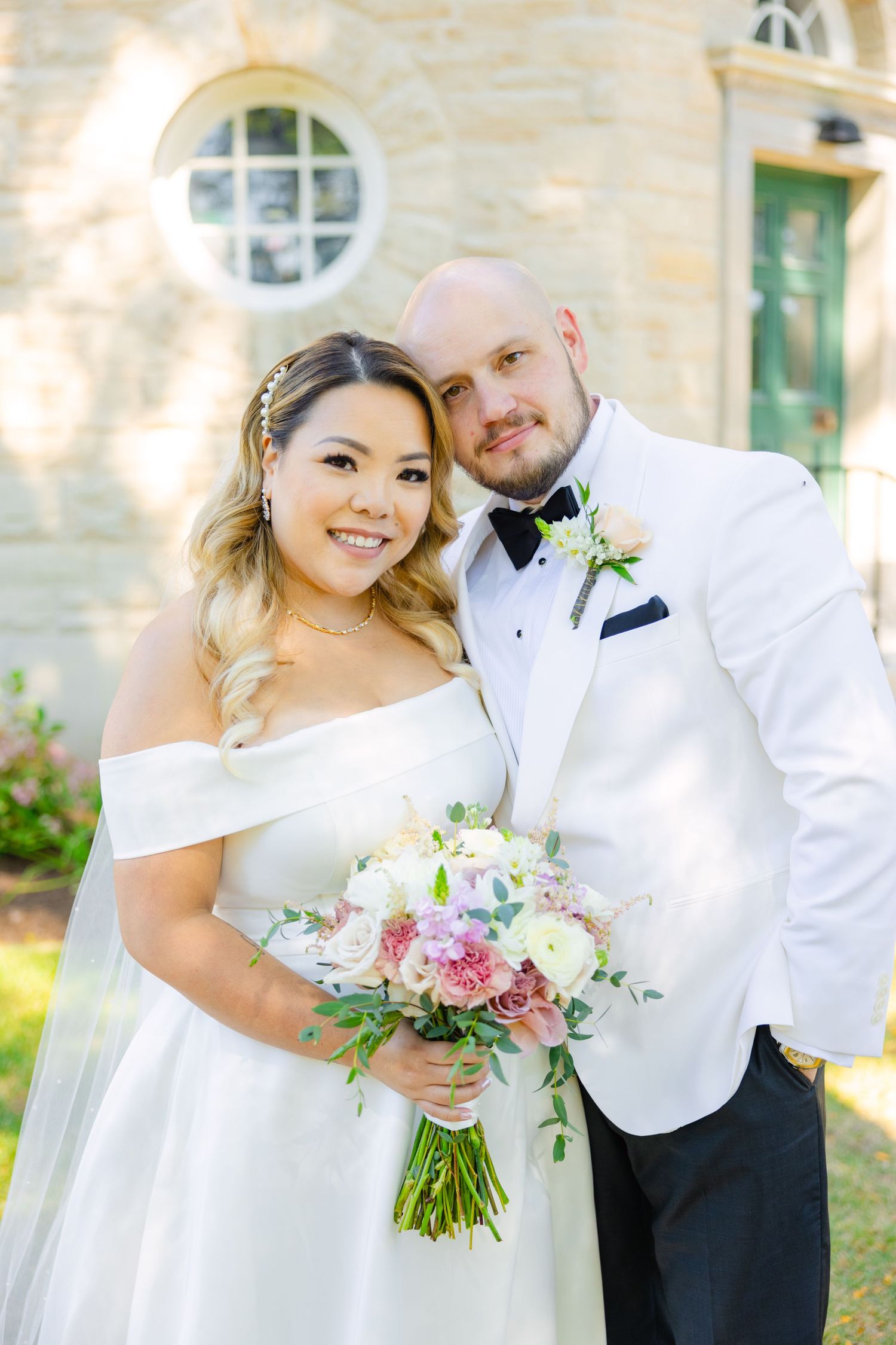 A happy wedding couple poses together against a stone building backdrop on their special day.