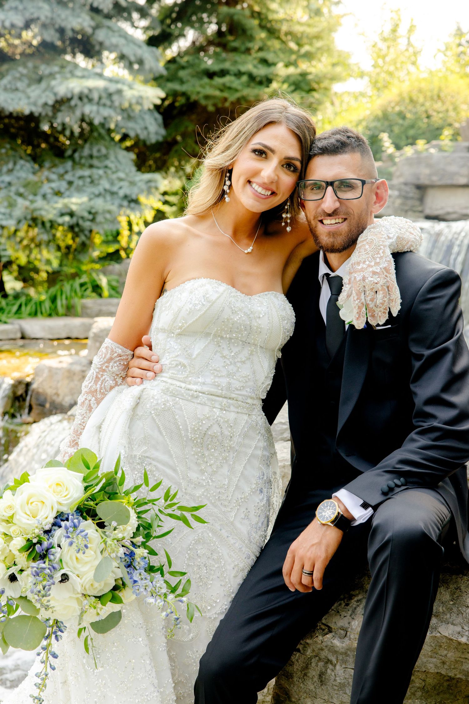 Romantic wedding portrait of newlyweds sitting on stone steps with waterfall backdrop.