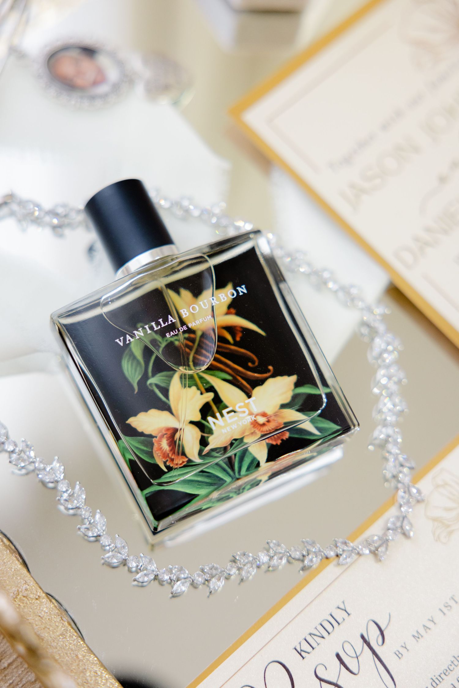 Elegant perfume bottle with floral design surrounded by crystal jewelry and wedding stationery.