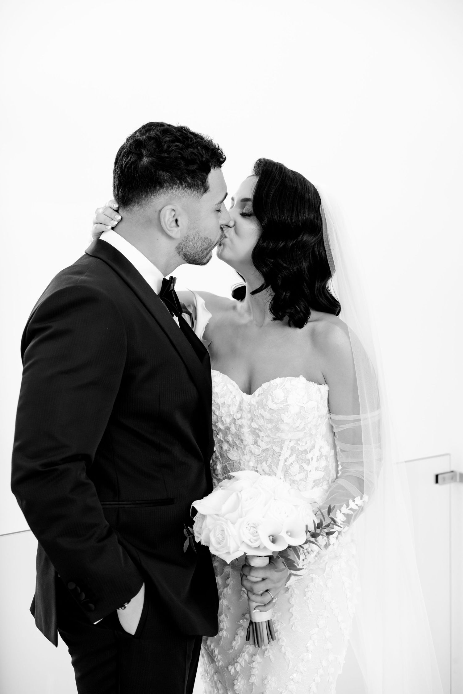 A romantic black and white wedding photo captures a couple sharing a tender kiss against a white background.