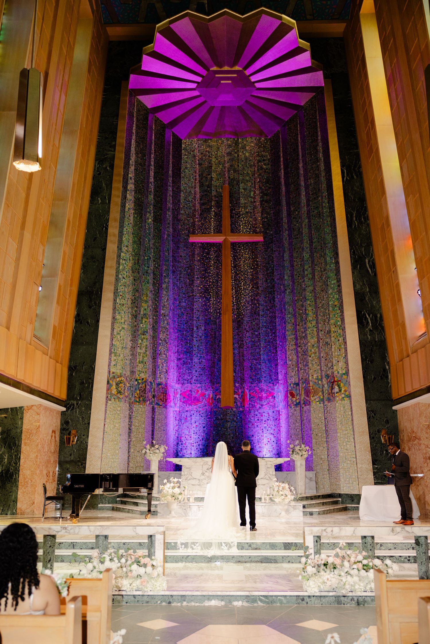 Church altar illuminated with vibrant purple lighting featuring geometric ceiling design and large cross.