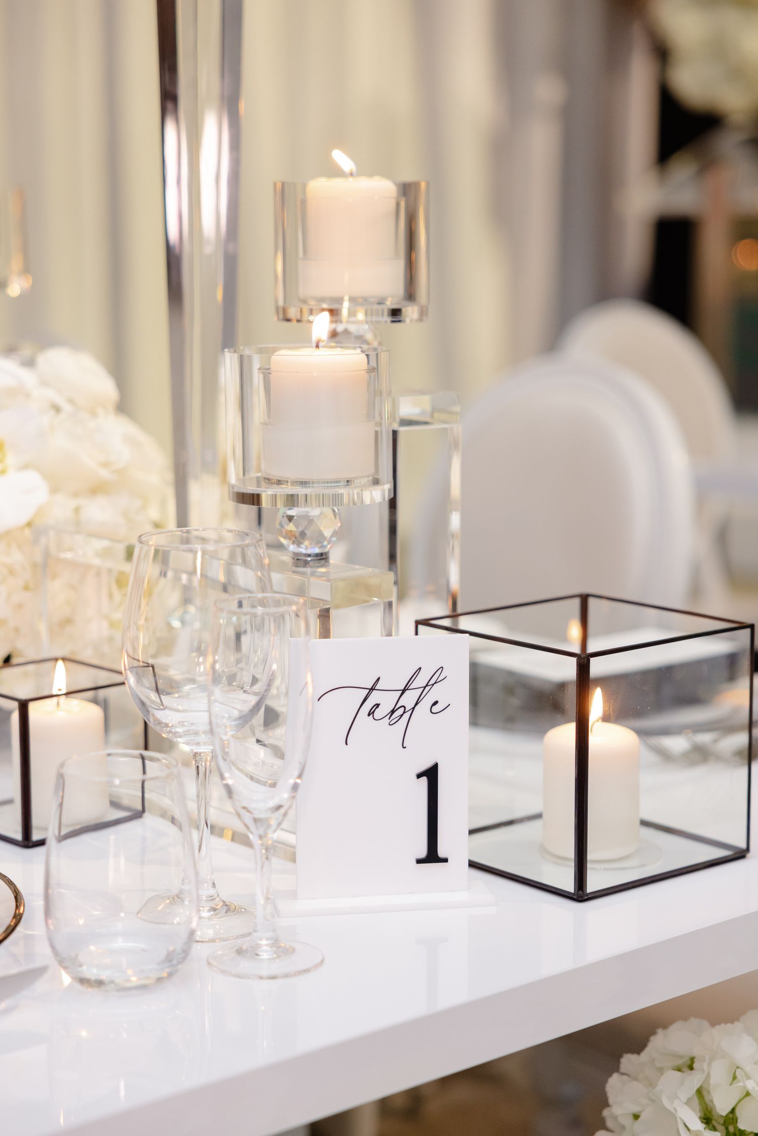 Elegant wedding table setting with crystal candleholders, table number one, and glass decor against white linens.