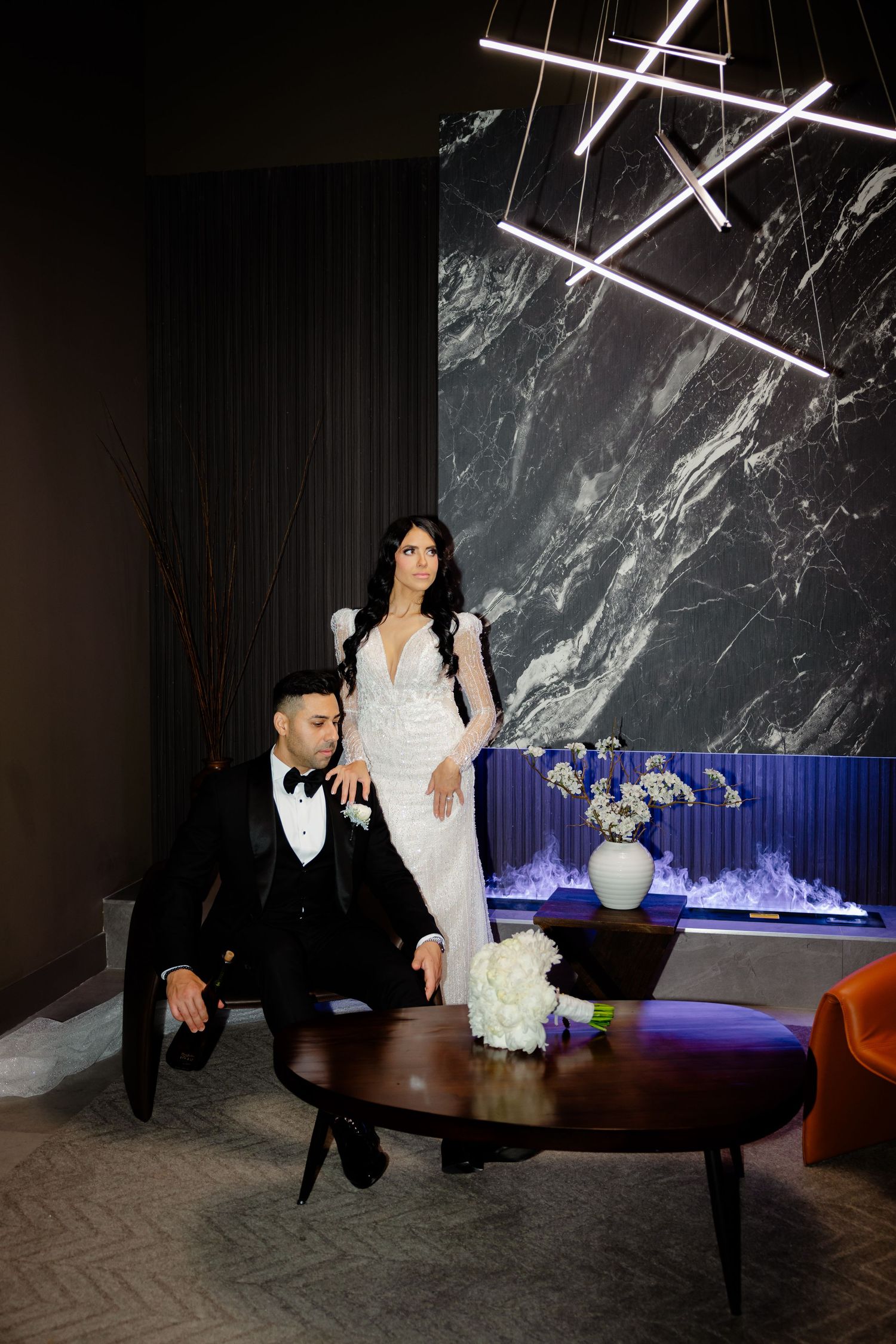 Wedding portrait in a modern space with dramatic lighting and marble wall backdrop.