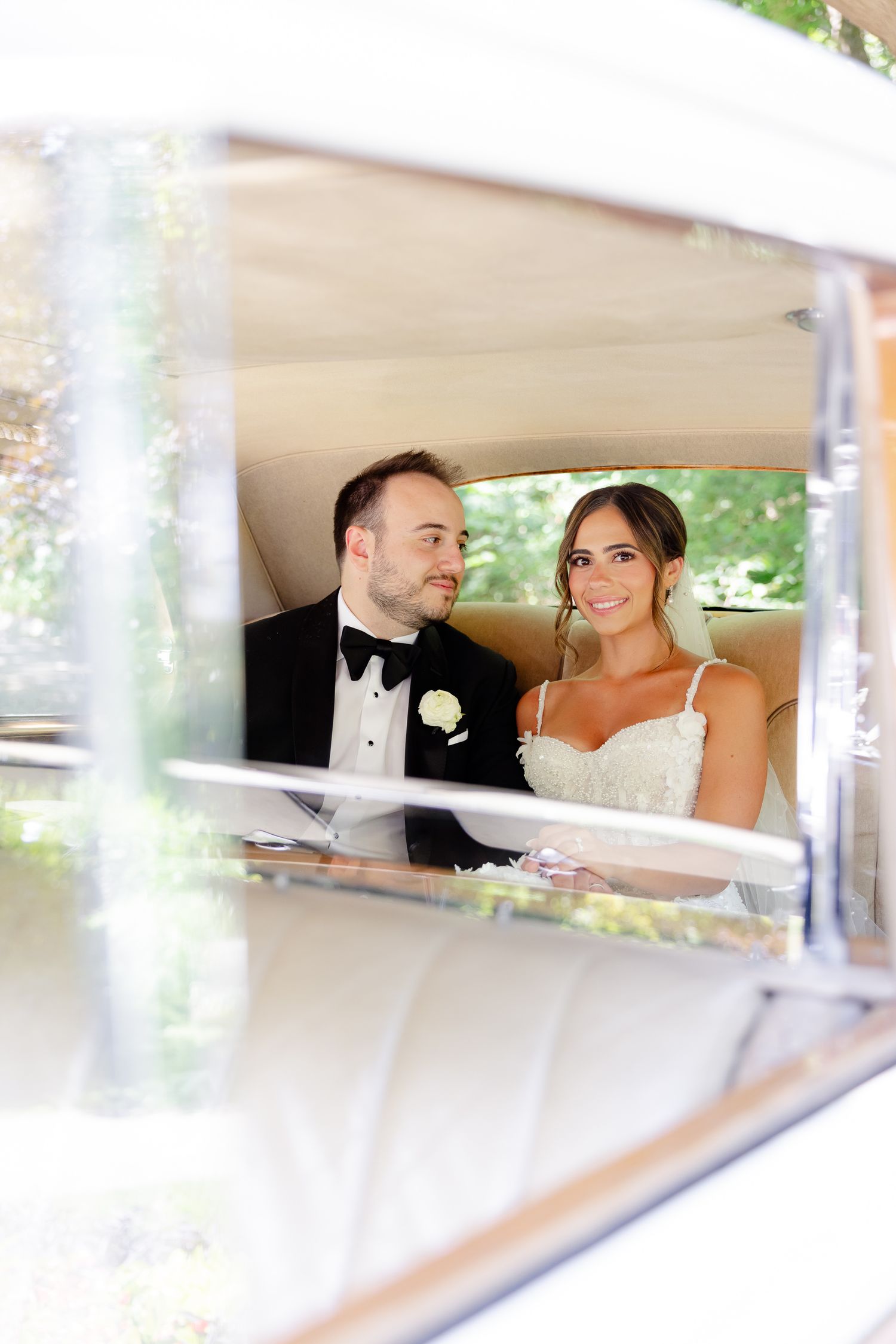 Newlywed couple shares a tender moment while sitting in classic wedding car interior.