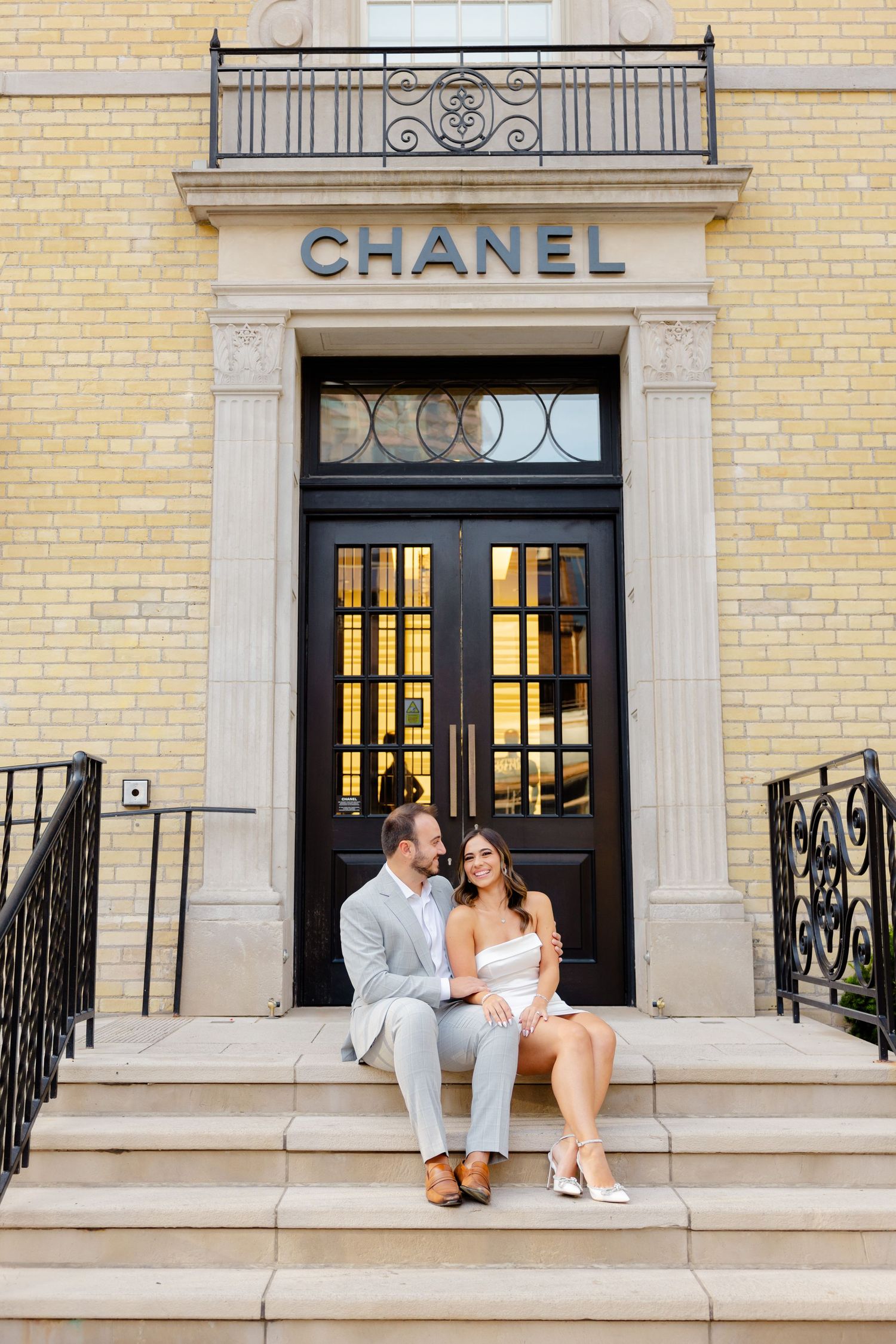 An elegant photo of a couple seated at the entrance of a Chanel store with ornate details.