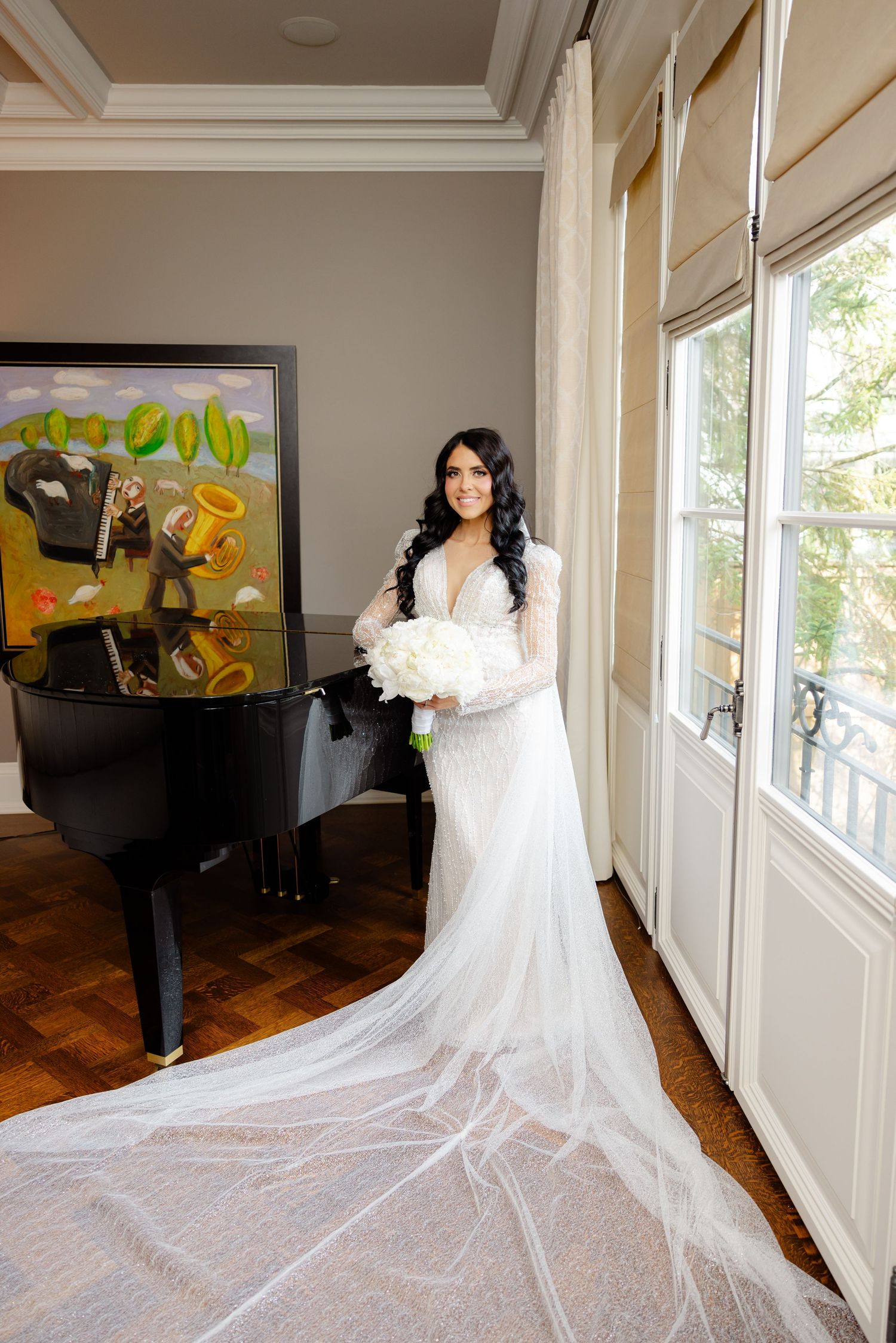 Elegant wedding dress with long train photographed in room with grand piano and modern art.