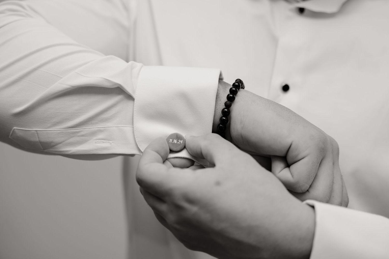 Hands adjusting cufflinks on white dress shirt sleeve.