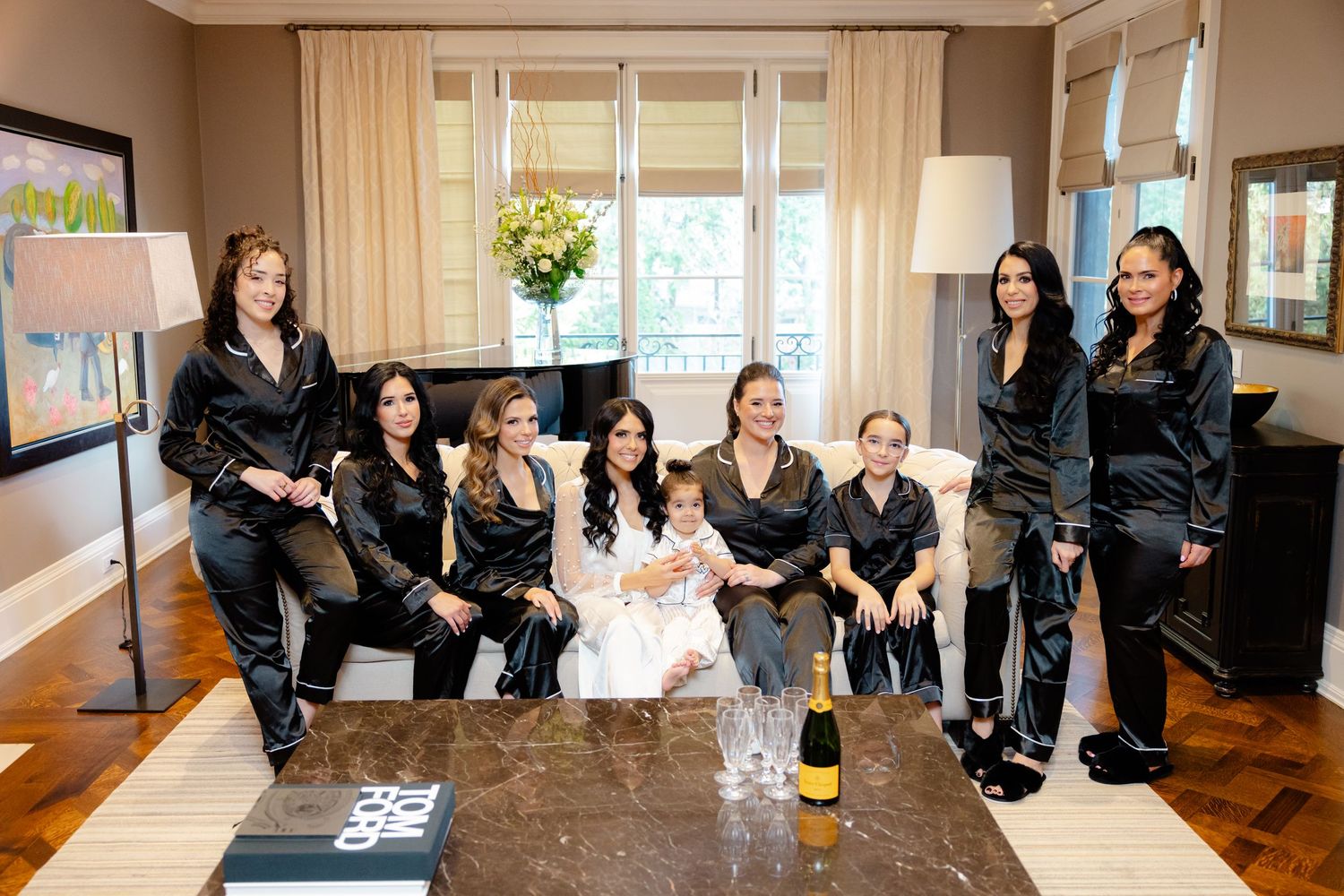 Wedding party in matching black robes gathered in living room for pre-ceremony preparations.