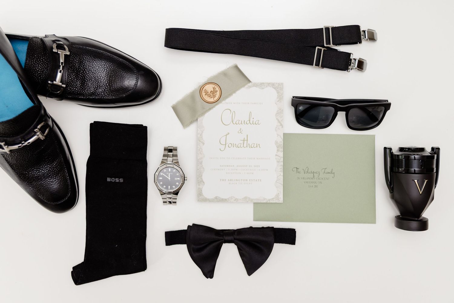 A collection of luxurious black and white wedding accessories including shoes, bow tie, watch, and invitation on light background.