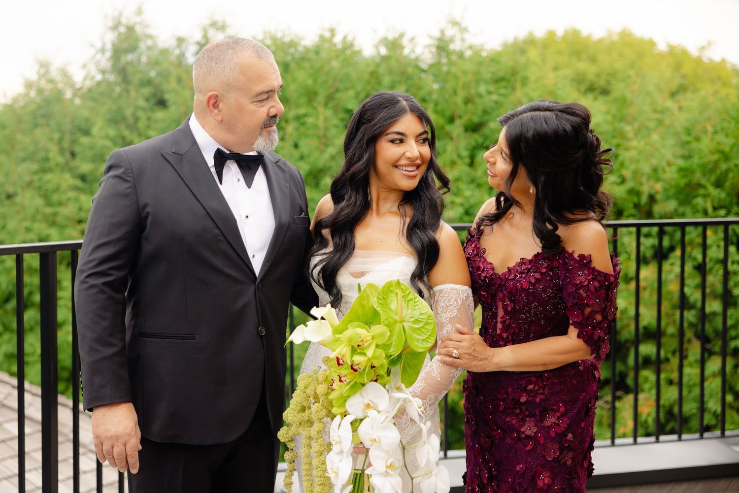 Well-dressed wedding party poses together on an outdoor balcony surrounded by lush greenery.