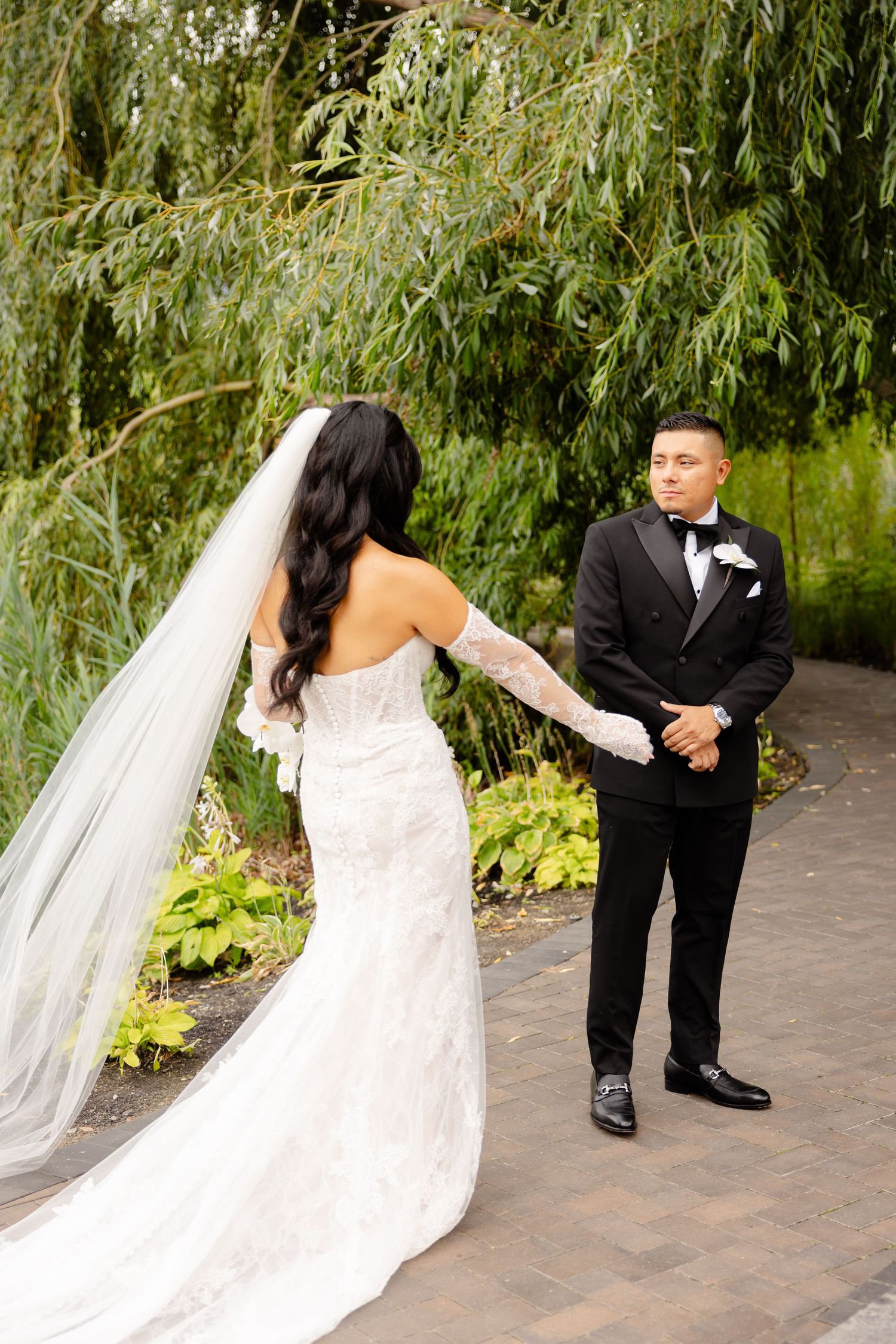 A wedding couple performs a romantic first dance sequence on an outdoor garden patio surrounded by weeping willows.