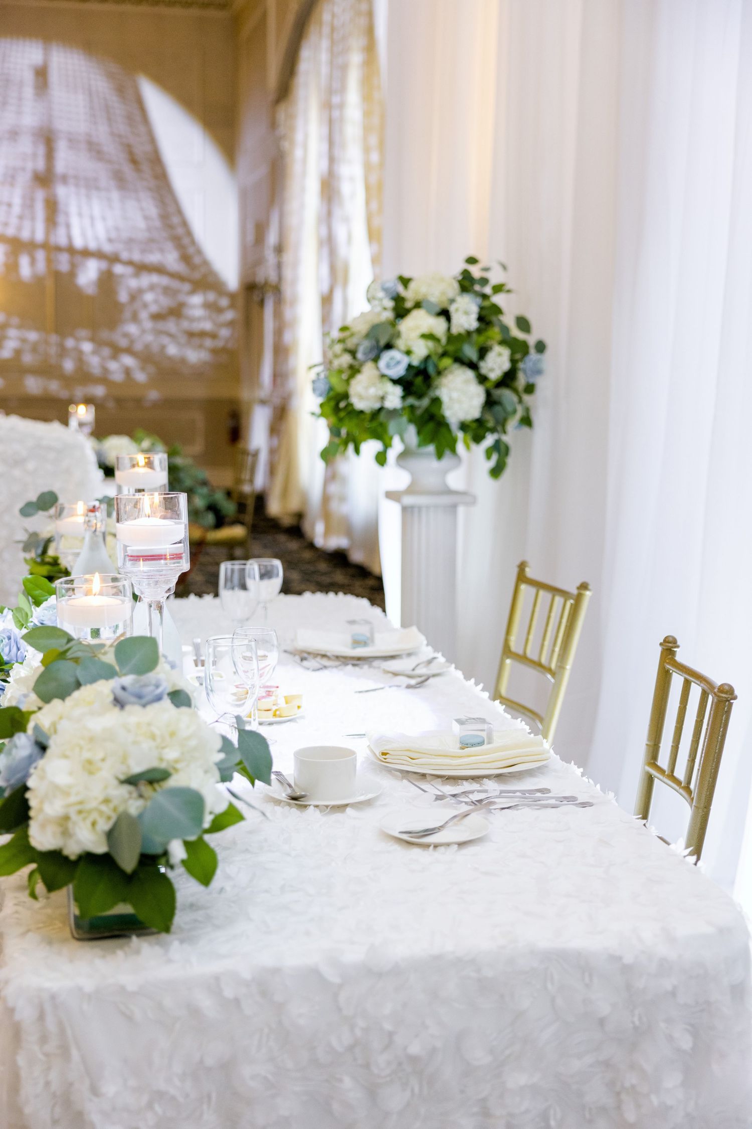 Elegant wedding table setting with white floral centerpieces and gold chiavari chairs.