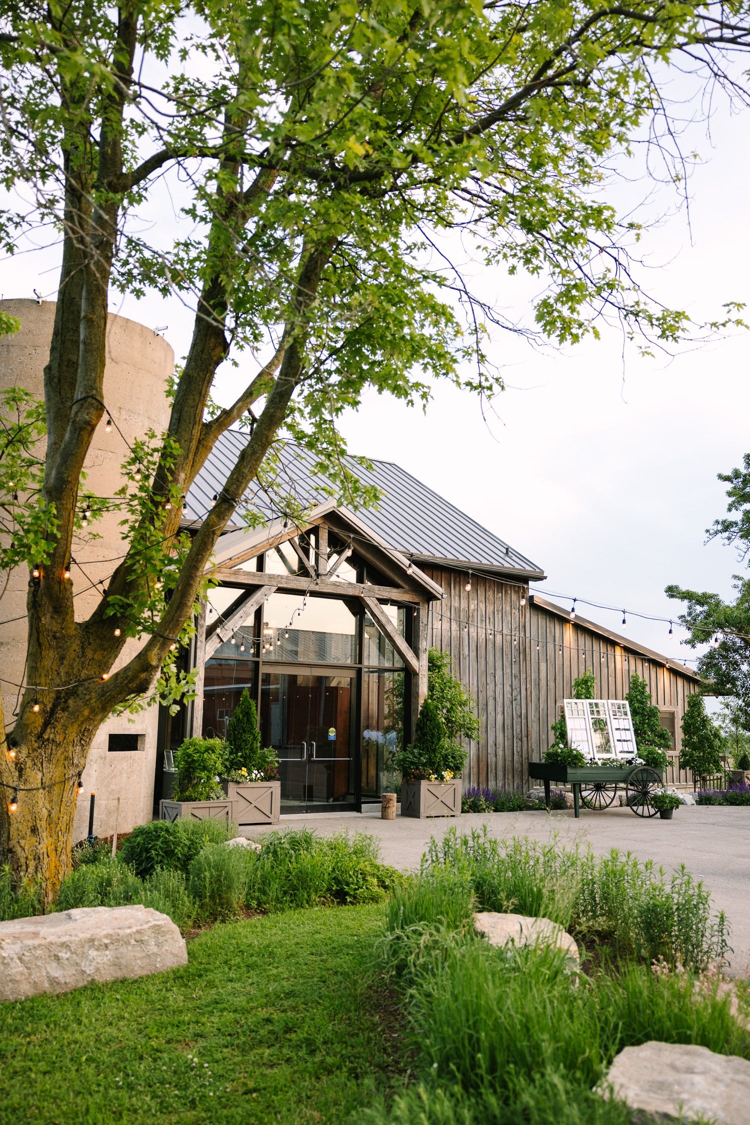 Rustic barn wedding venue exterior with lush green trees and landscaping.