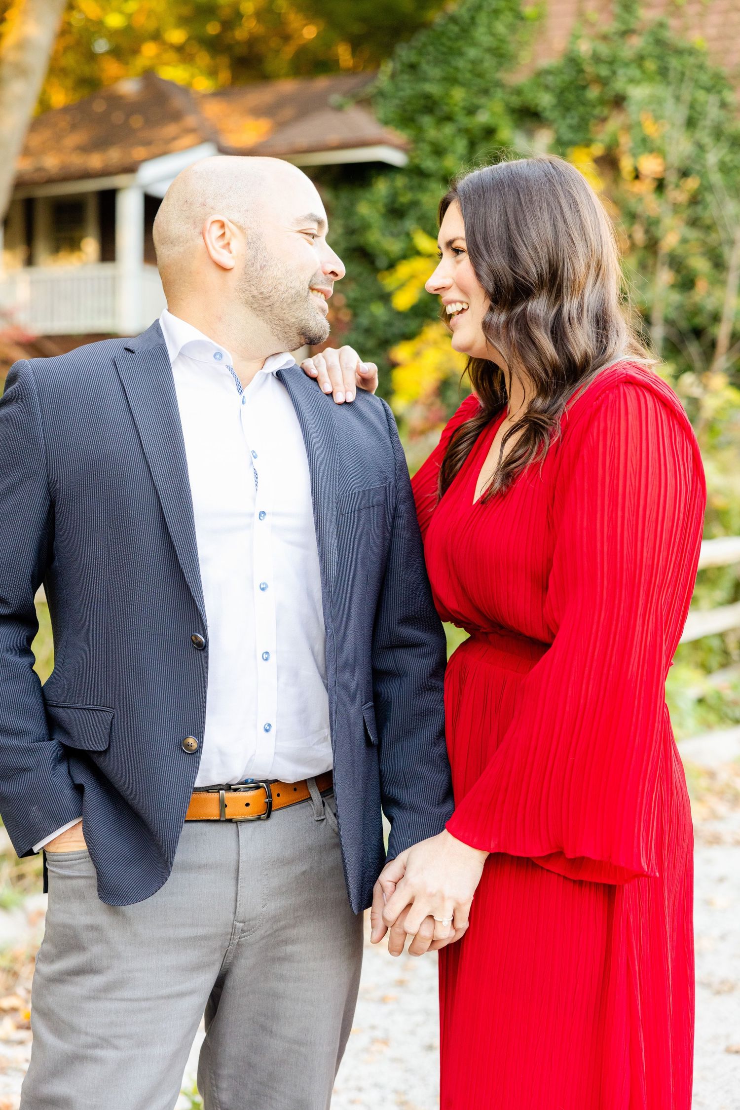 Joyful couple laughing together outdoors in formal attire during fall photoshoot.