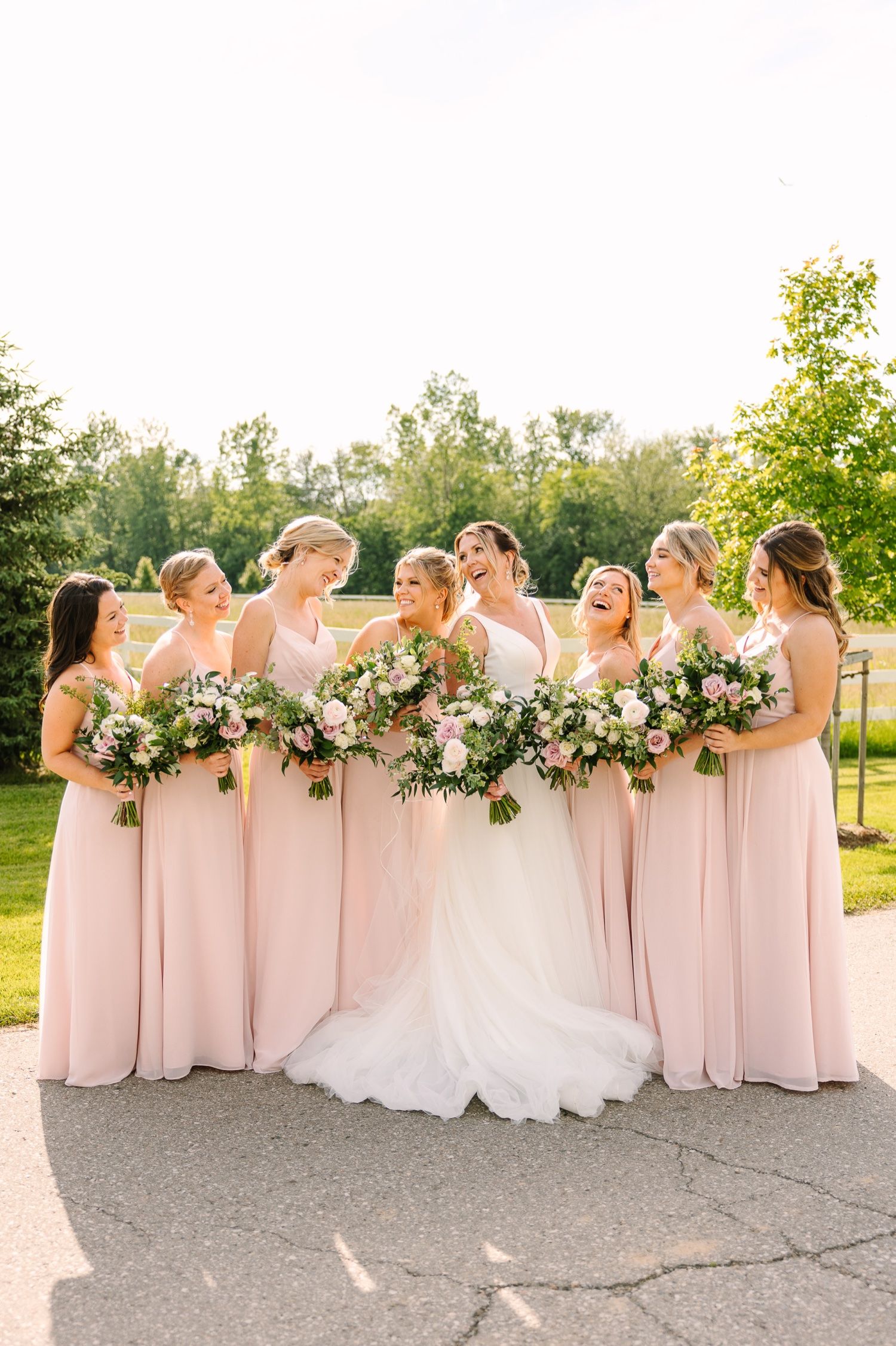 Bridesmaids in matching pink gowns gather around the bride holding elegant floral bouquets.