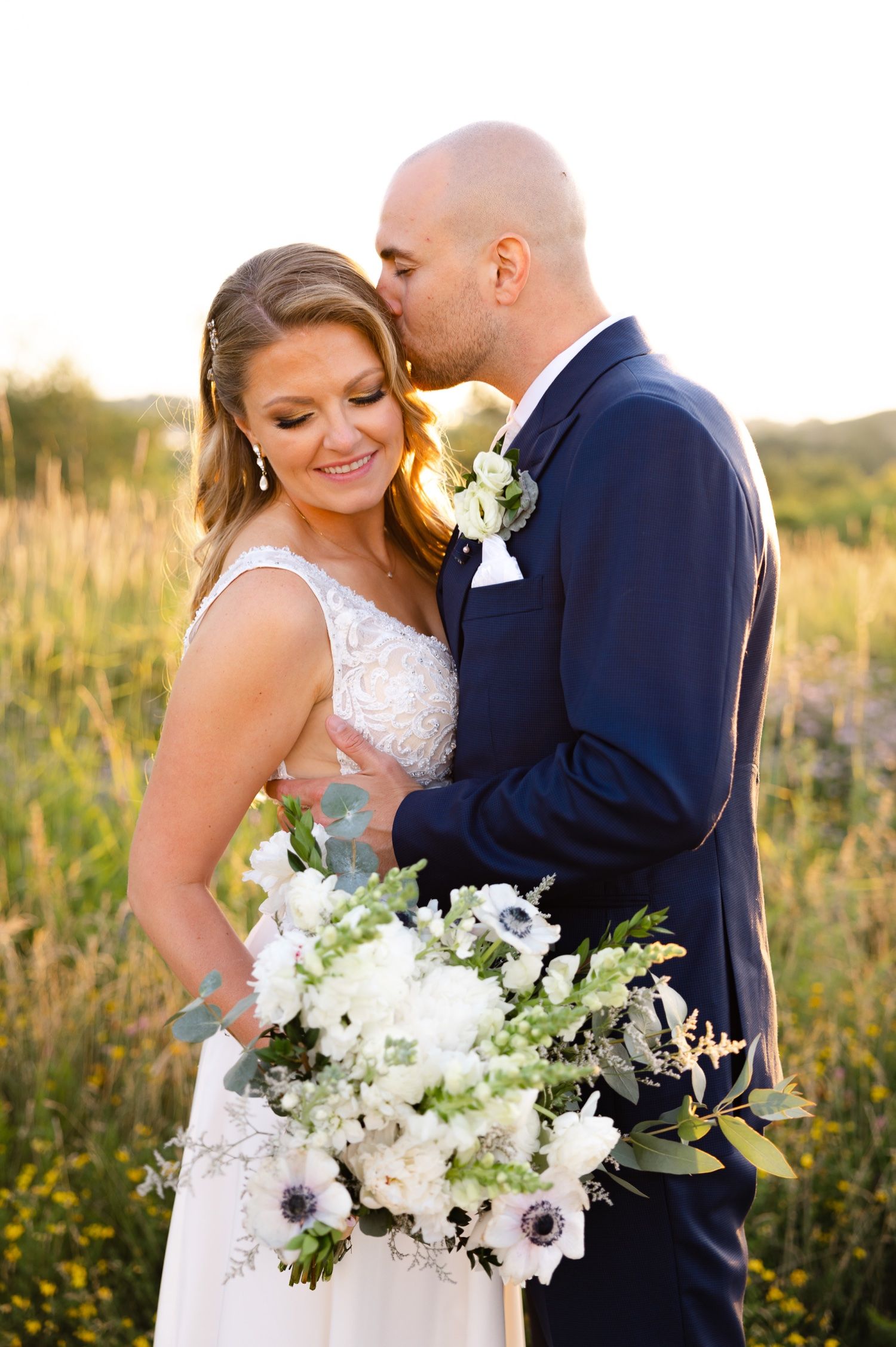 A tender moment between newlyweds in a golden field with white wedding flowers.