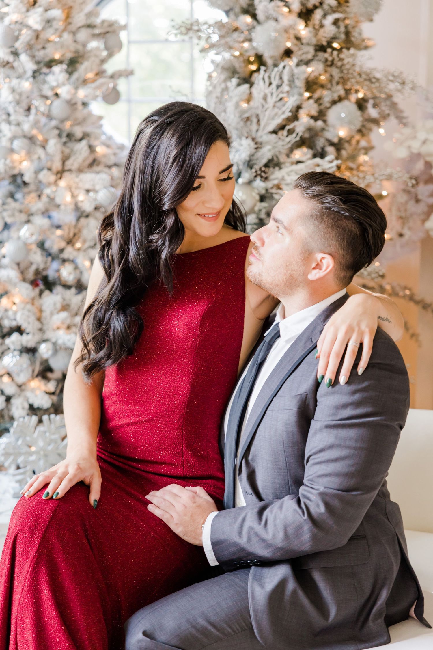 Intimate moment captured between couple in formal wear by snow-flocked Christmas tree.